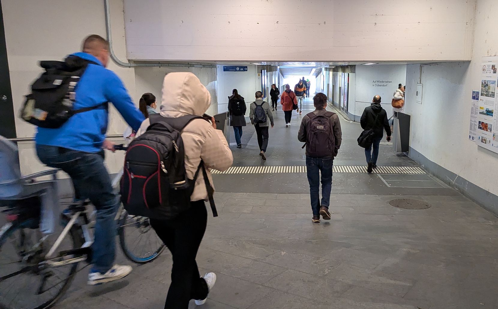 Man sieht eine düstere Bahnhofunterführung mit Passanten und Velofahrern.