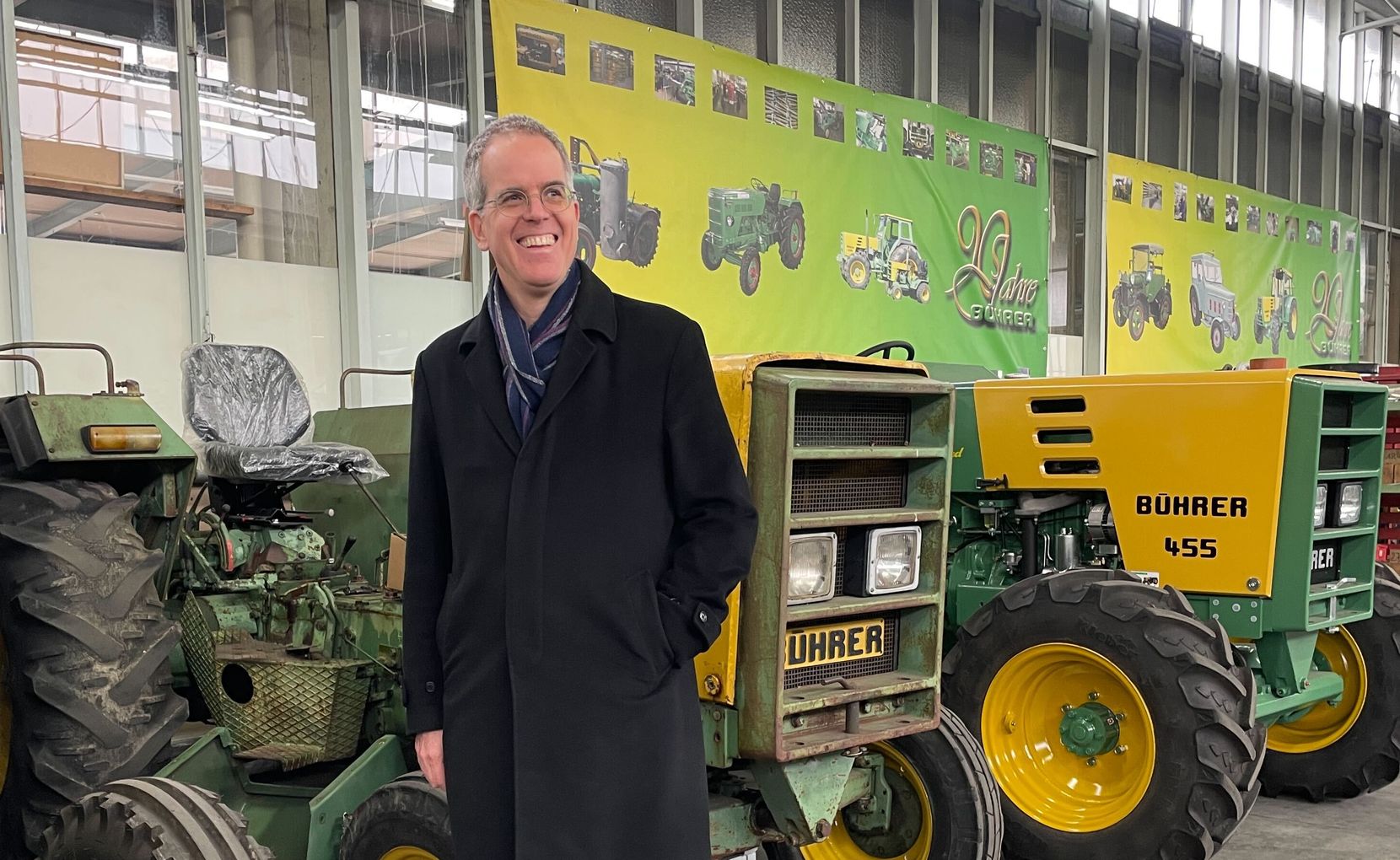 Man sieht Michel Eichenberger vor den neuesten Modellen der Bührer-Traktoren mit einem grossen Grinsen.