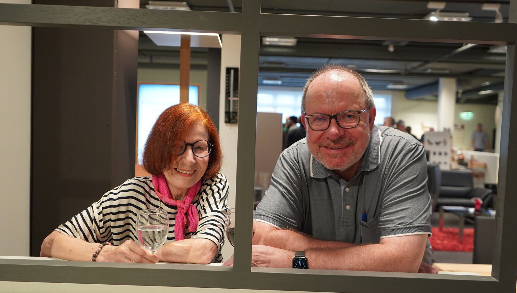 Ein Mann und eine Frau schauen durch einen Rahmen und lächeln in die Kamera.