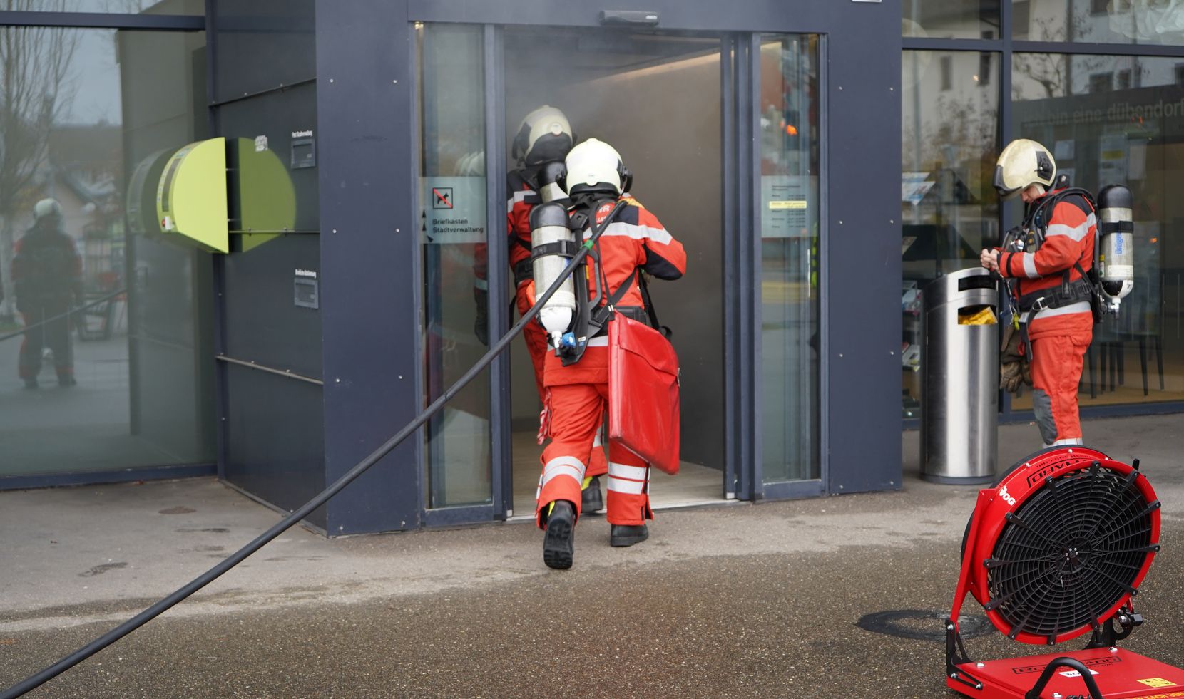 Zwei Feuerwehrleute laufen mit einem Wasserschlauch in das verrauchte Stadthaus.