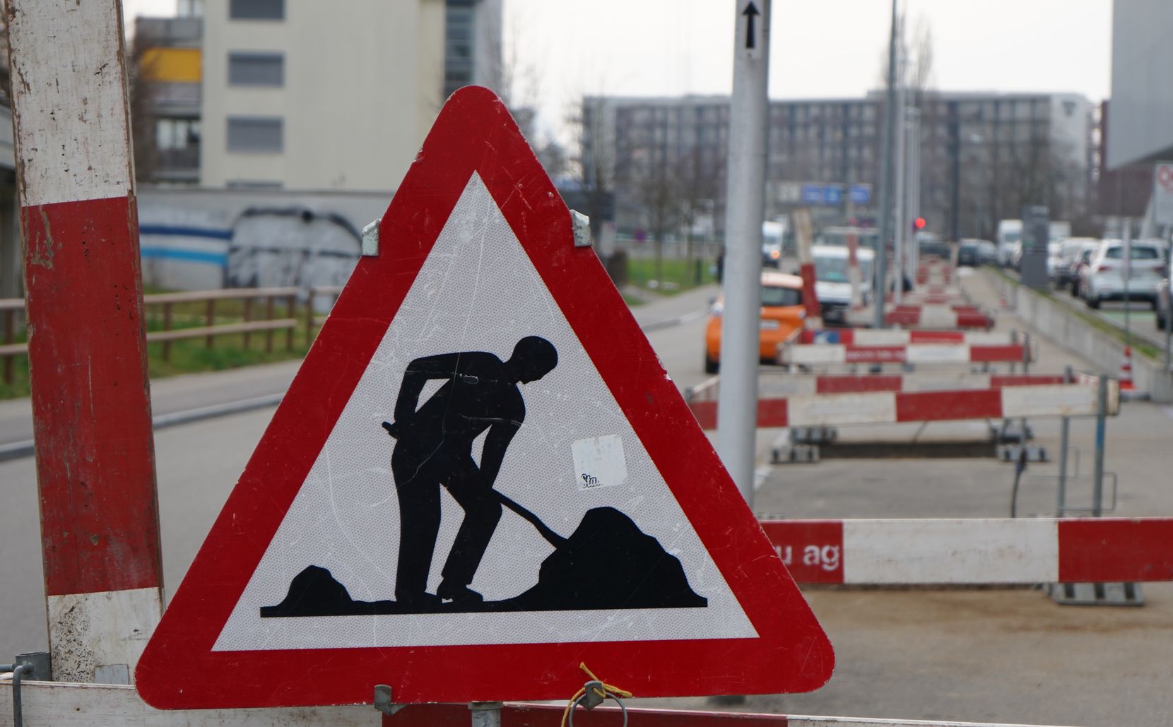 Baustelle mit Hinweistafel und rot-weissen Abschrankungen.