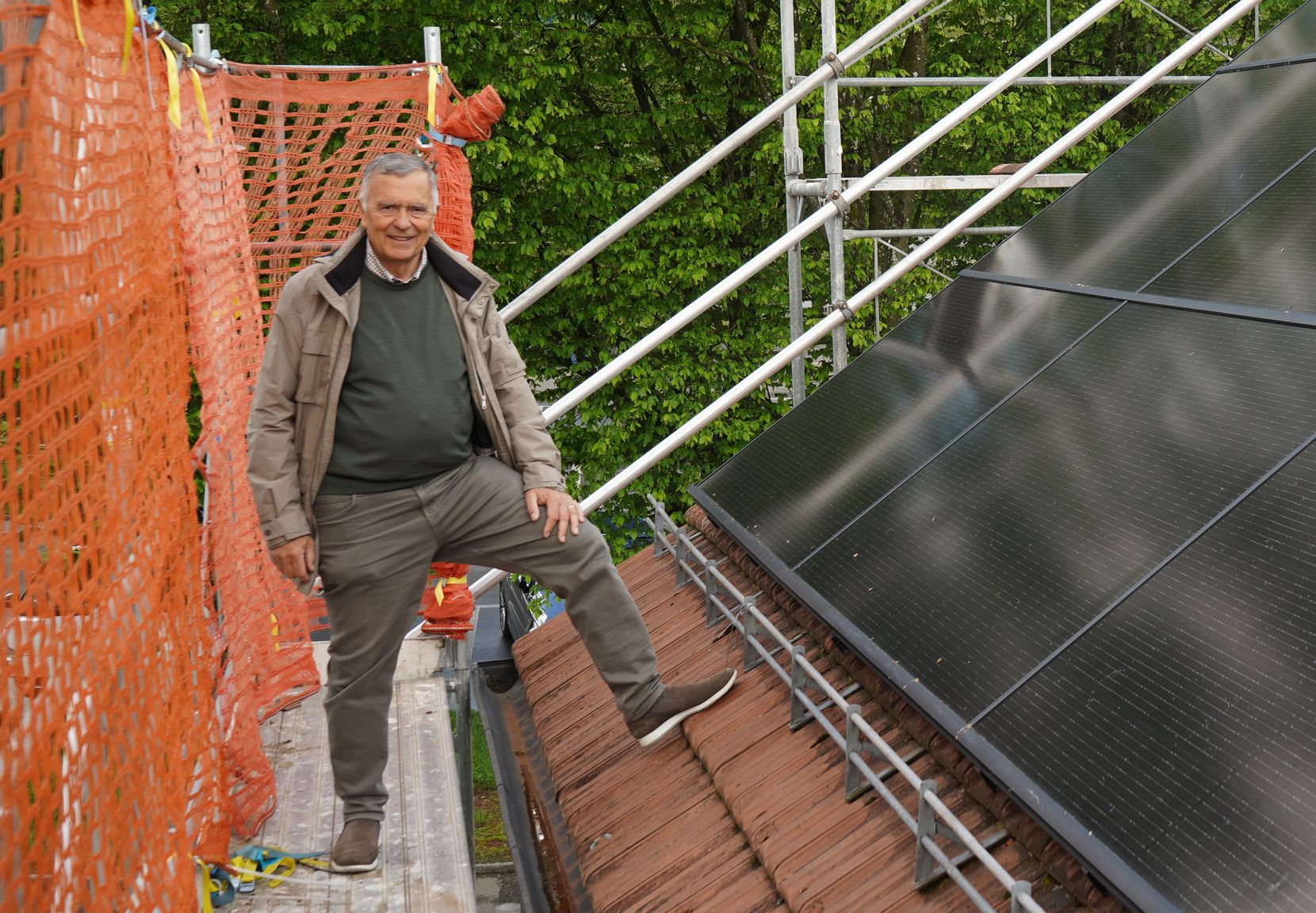 Ein Mann steht auf einem Gerüst neben einer auf dem Dach montierten Solaranlage und lächelt in die Kamera
