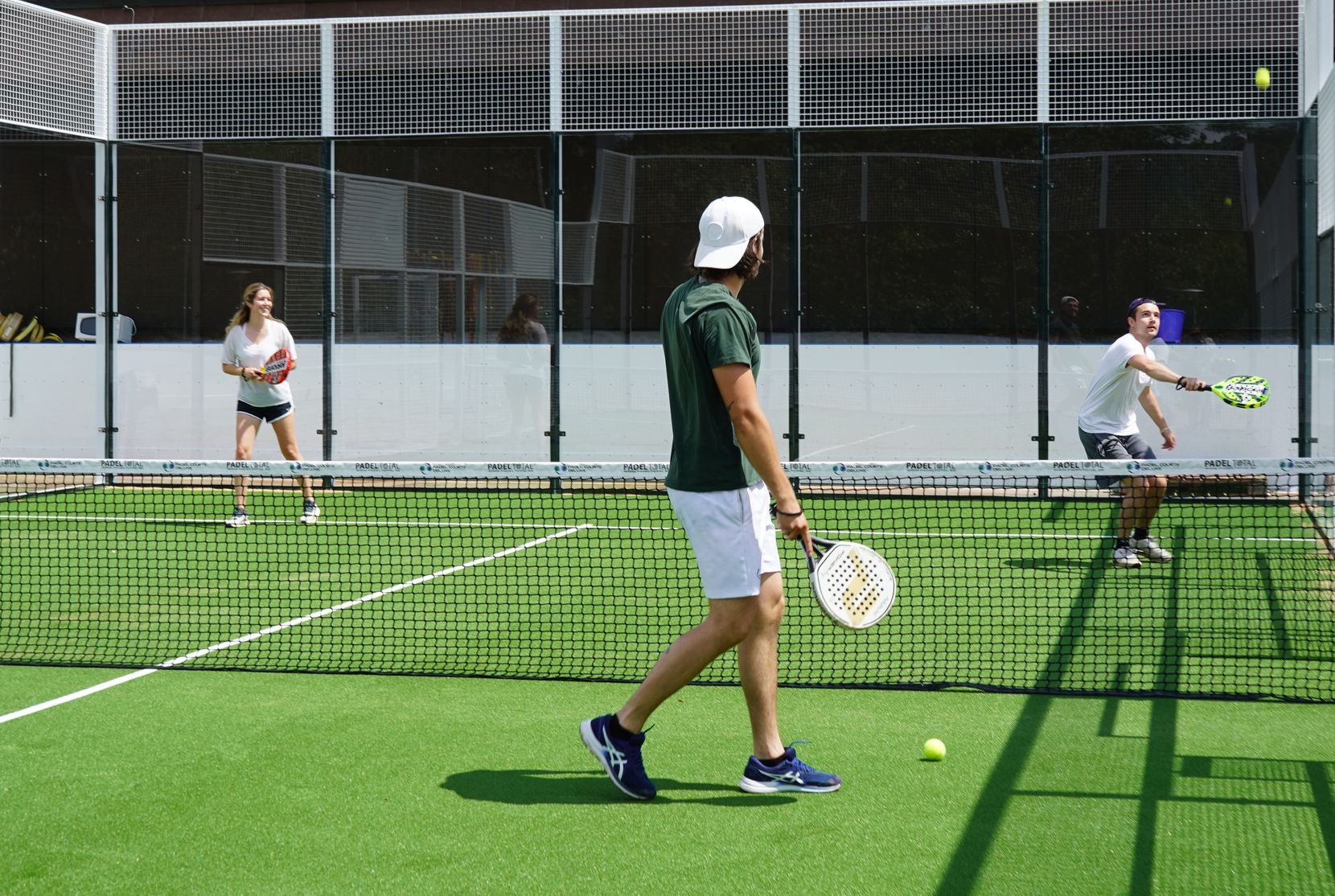 Zwei Männer und eine Frau spielen eine Art Tennis auf einem Feld. 