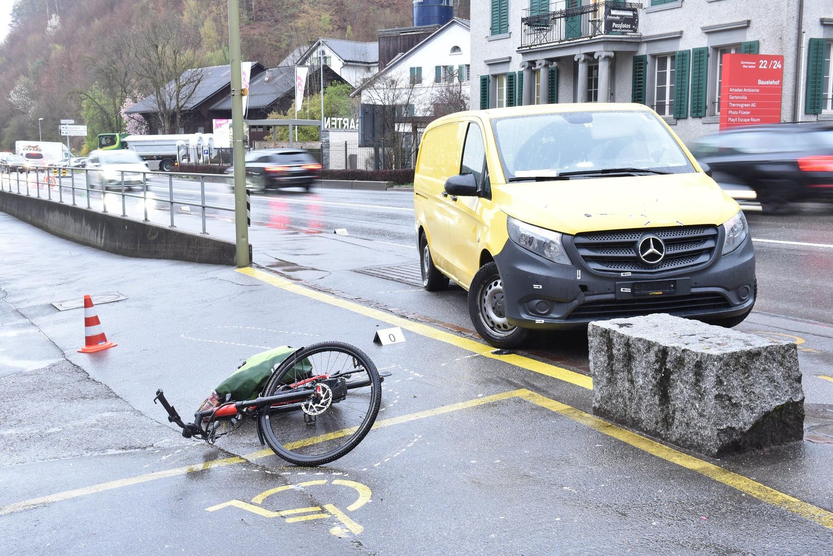 Ein grünes E-Bike liegt auf der Seite auf dem Asphalt. Im Hintergrund ein gelber Transporter.