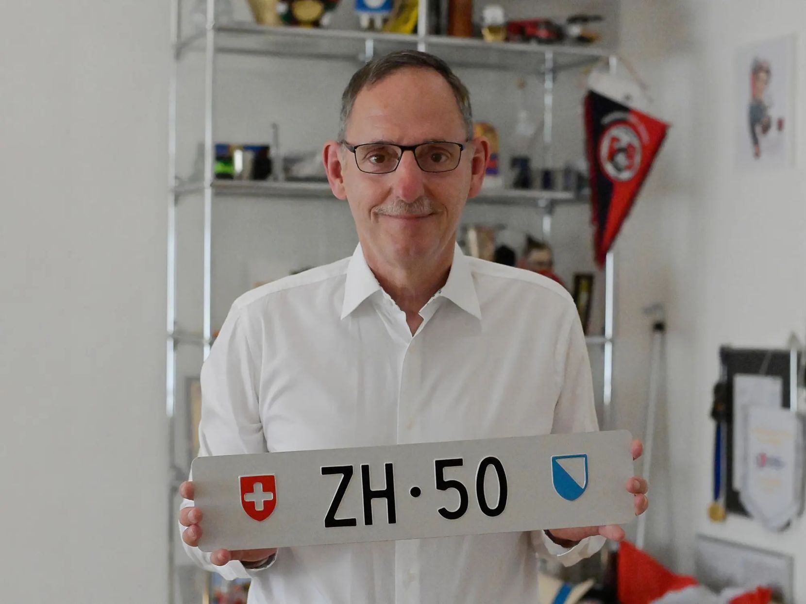 Alter Mann mit Brille hält Kontrollschild mit der Aufschrift ZH 50.
