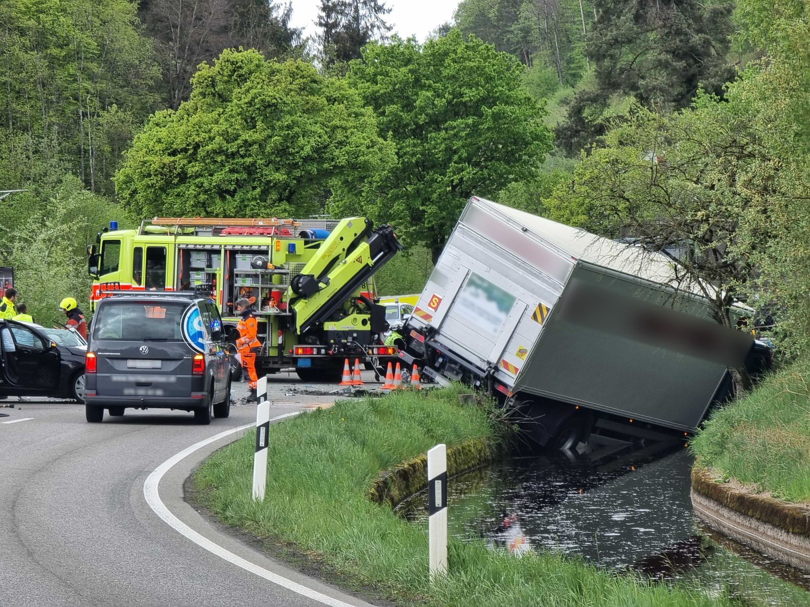 Verkehrsunfall in einer Kurve im Aatal. Ein Lastwagen liegt mit dem Vorderteil im Bach. Feuerwehrwagen und Einsatzkräfte vor Ort.