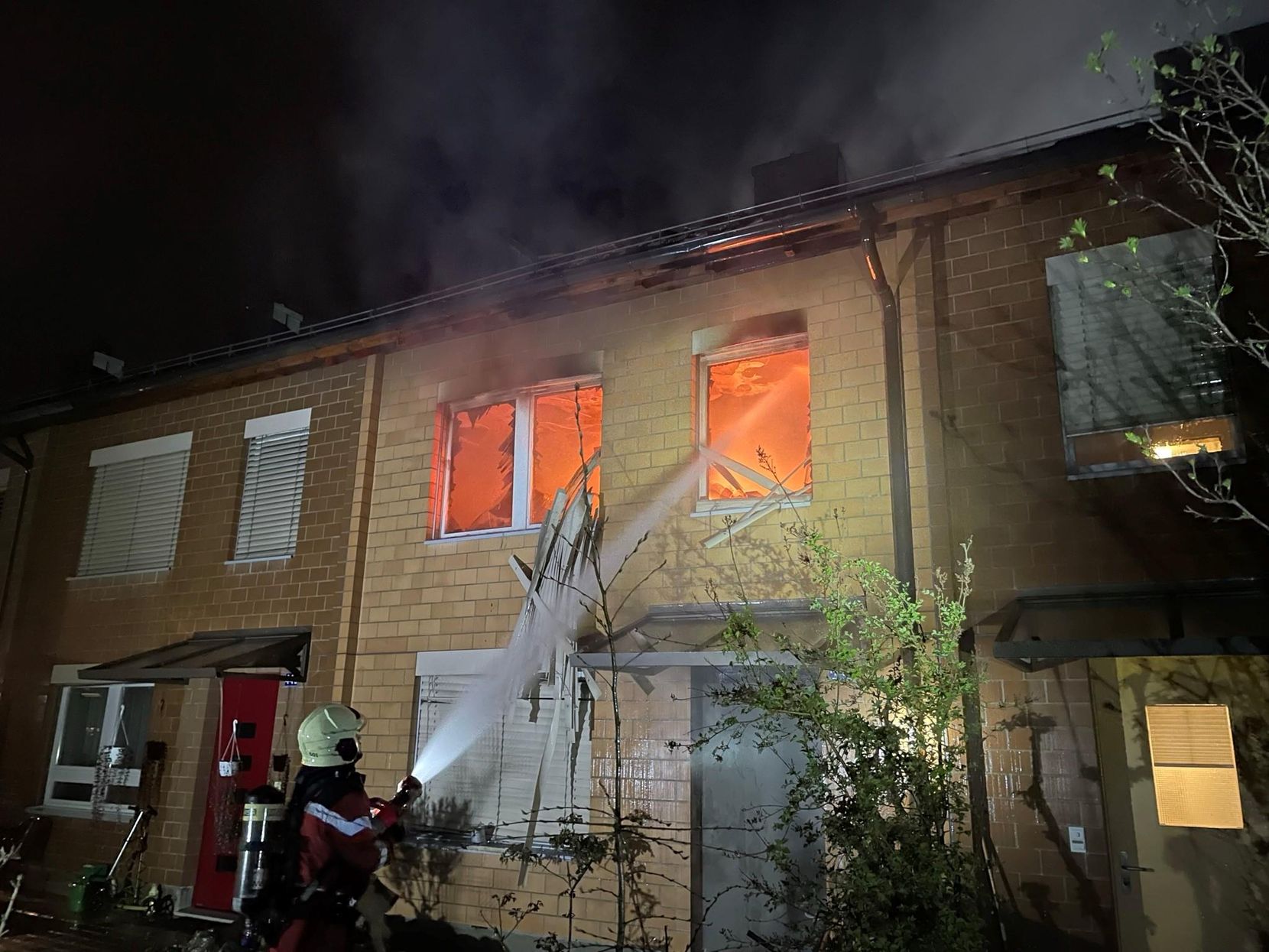 Ein Feuerwehrmann spritzt Wasser von aussen durch ein Fenster in eine brennende Wohnung