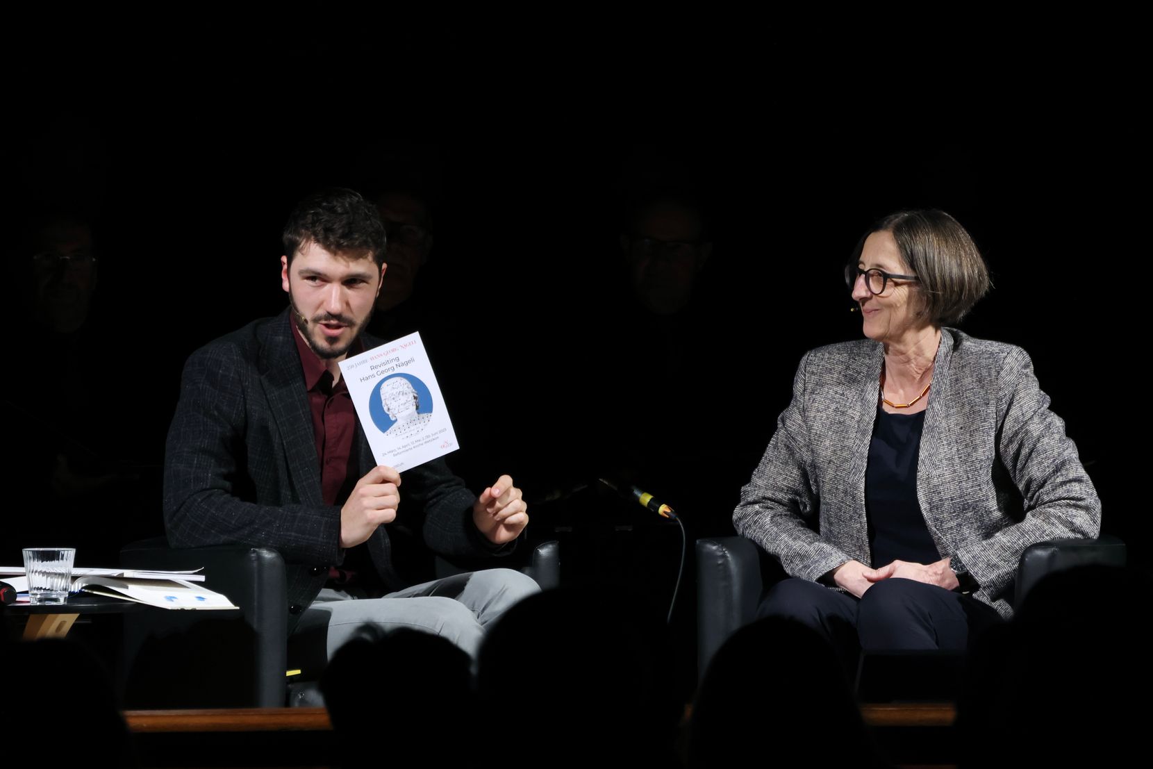 Historiker Andrea Schmid mit Buch in der Hand und Claudia Fischer-Karrer, beide sitzend auf einem Stuhl.