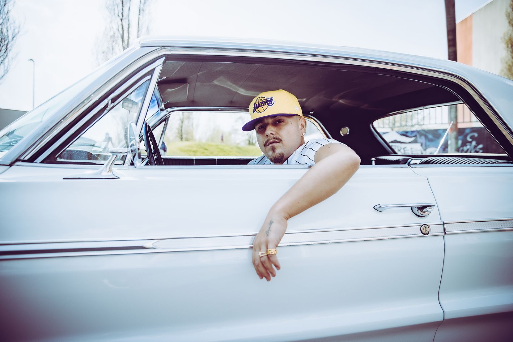 Junger Mann mit Basecap in einem weissen Oldtimer sitzend – die Hand aus der Tür hängend.