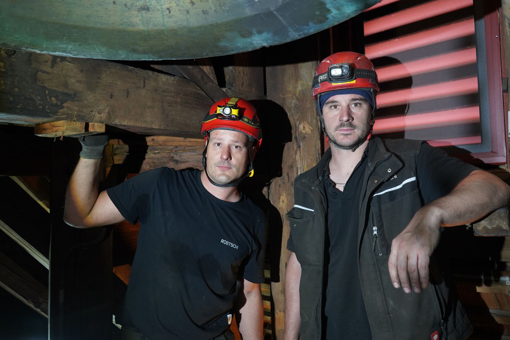 Zwei Männer mit Helmen und Stirnlampen in einem dunklen Dachstock.