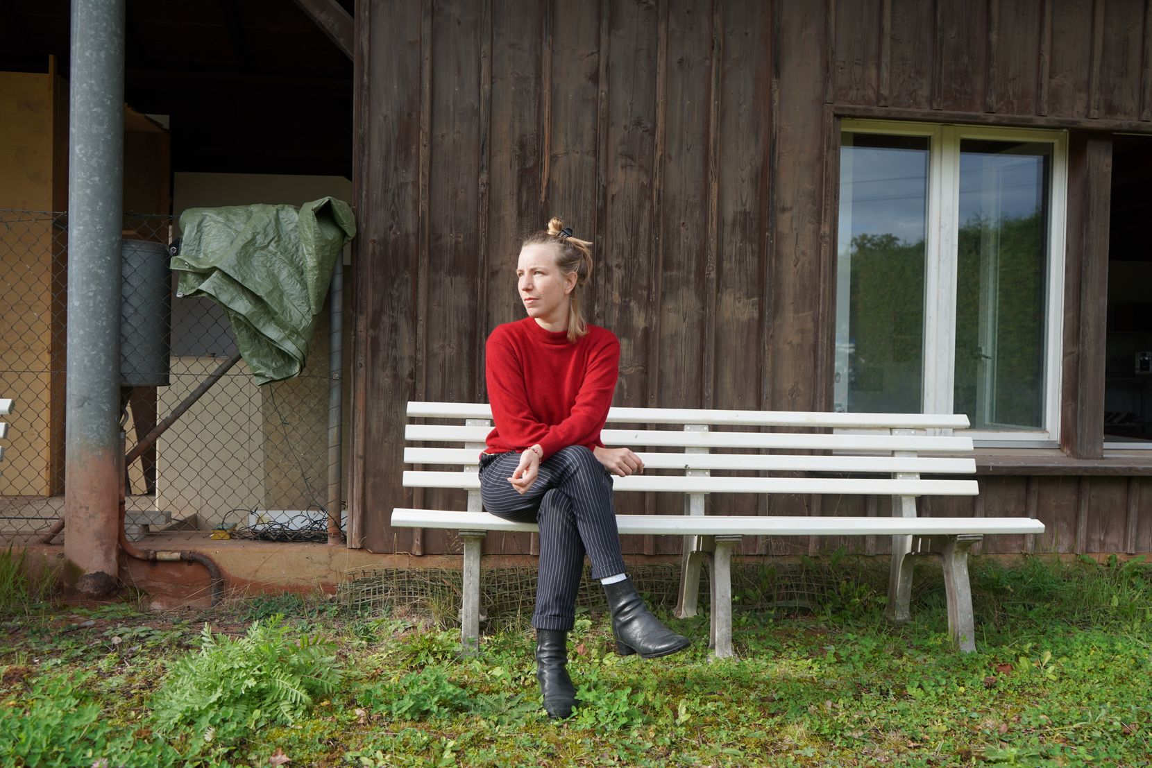 Eine Frau im roten Pulli sitzt auf einer Bank vor einem Haus.