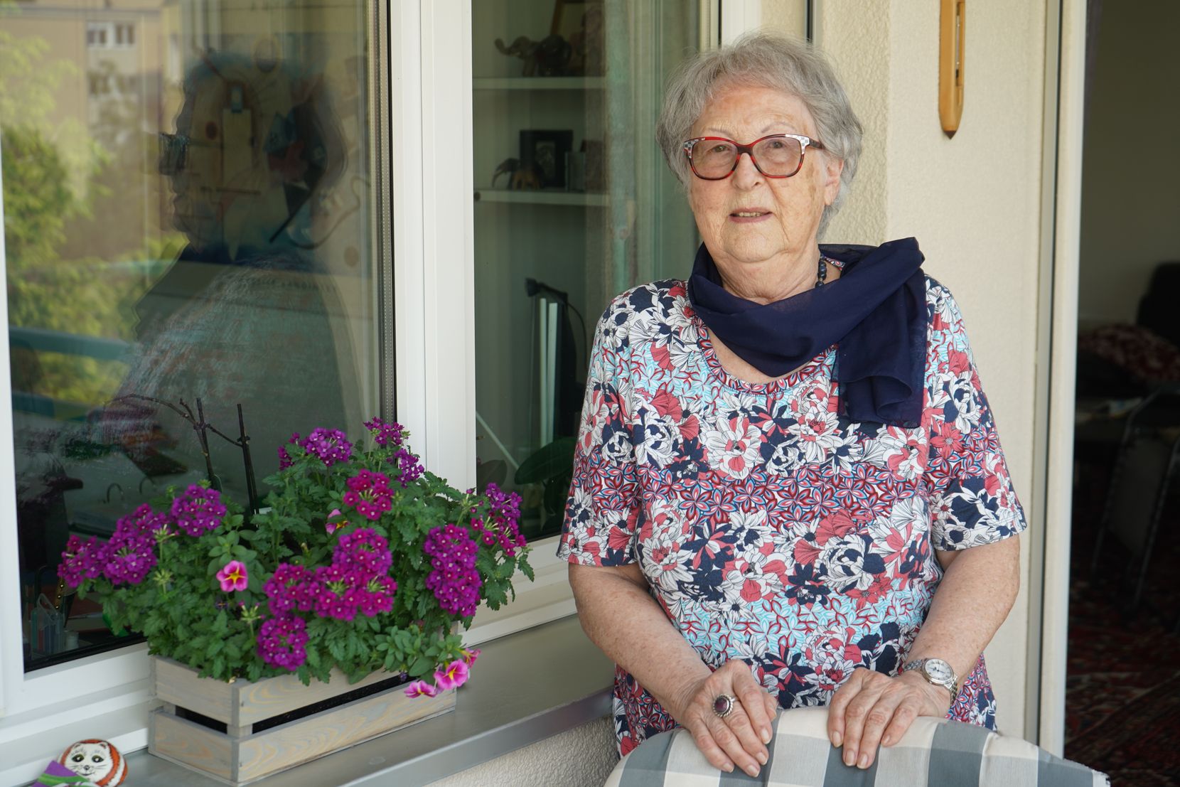 Eine Seniorin steht auf einem Balkon.