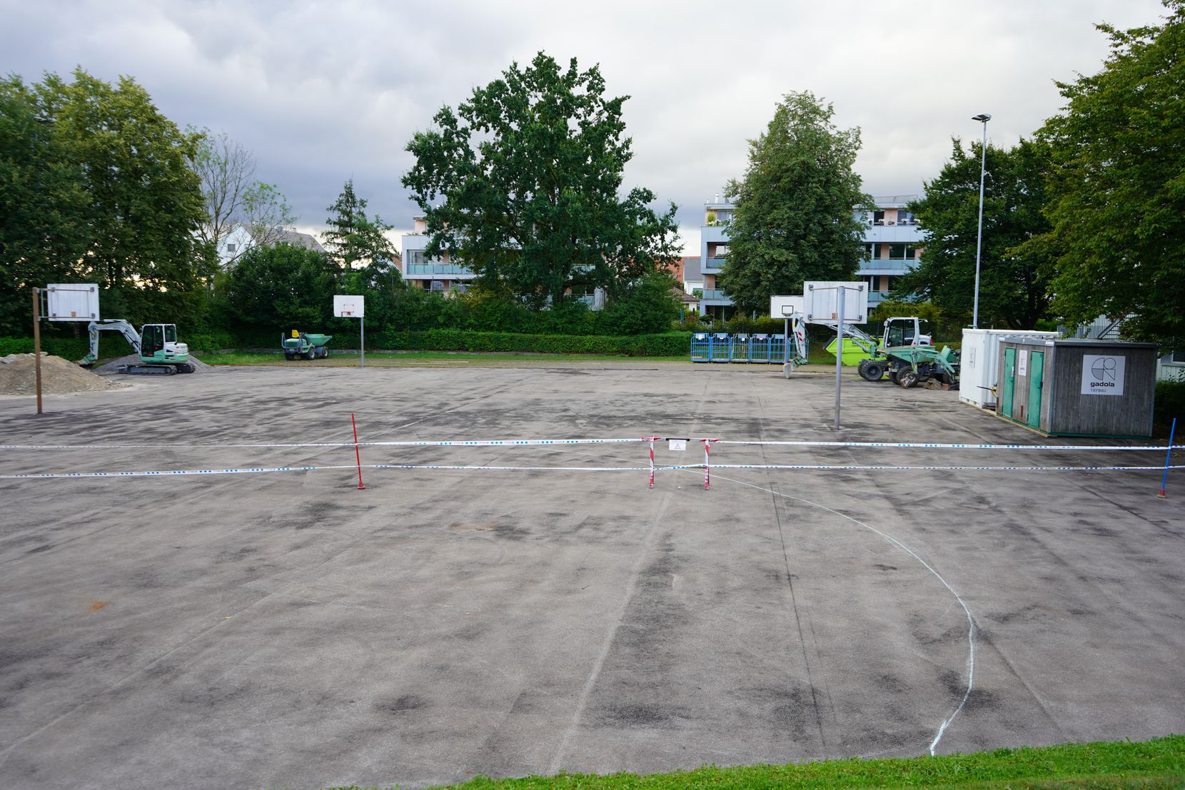 Ein Platz mit Basketballkörben und Baumaschinen.