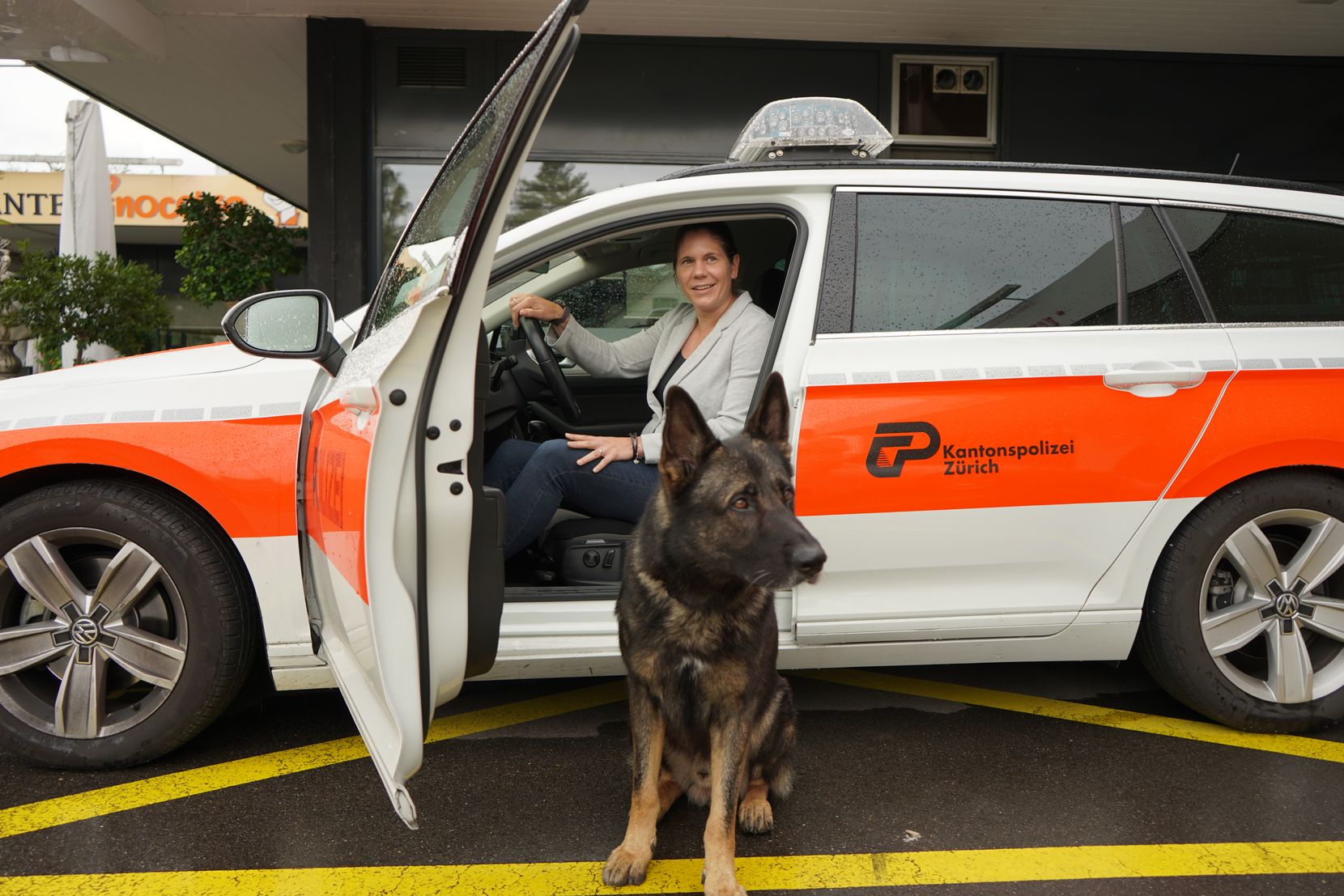 Eine Frau und ein Polizeihund vor einem Polizeiauto.