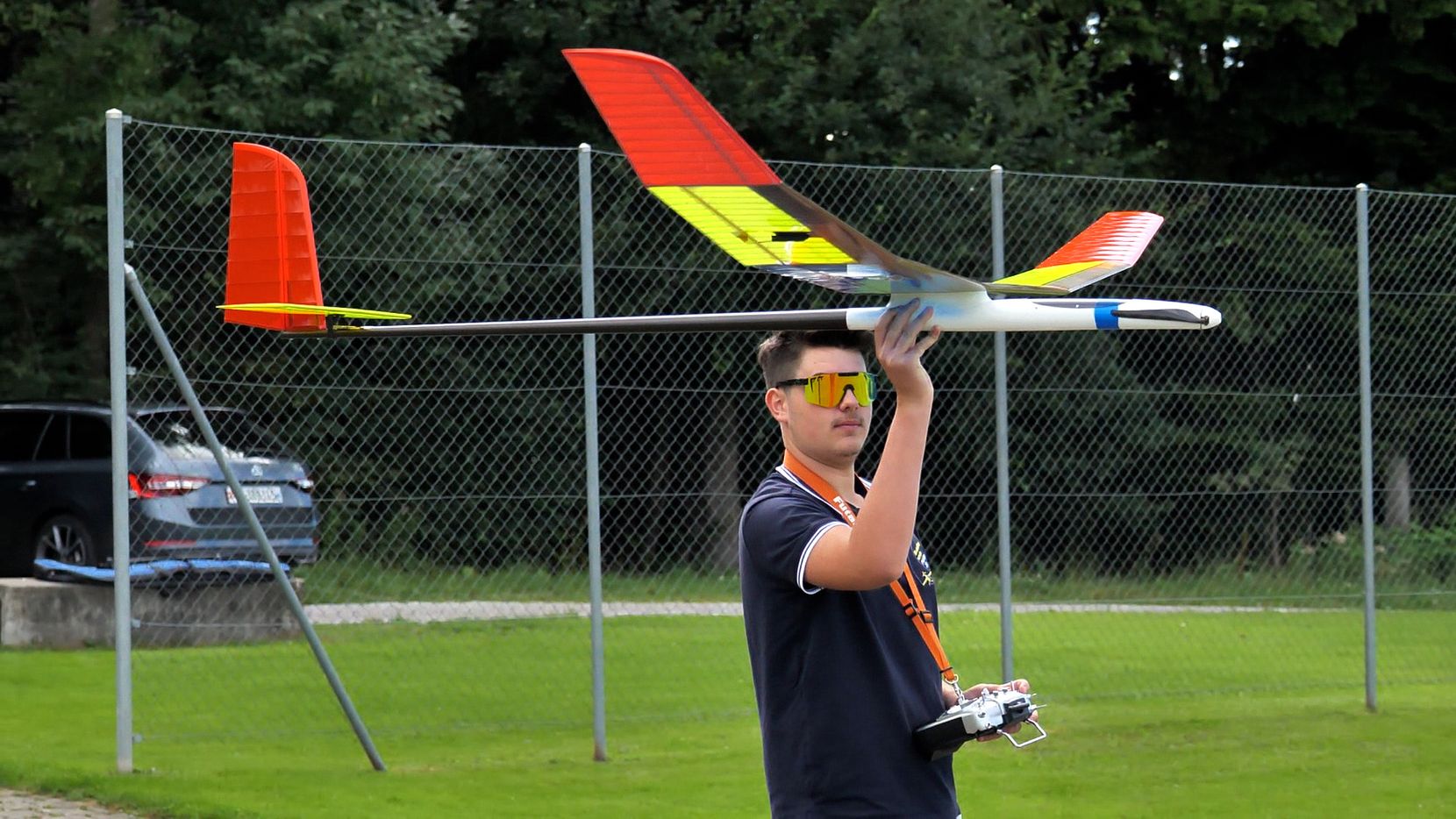 Auf dem Bild ist ein Mann mit einem Modellflieger und einer Fernsteuerung in der Hand, der sich auf dem Flugplatz Längi befindet.