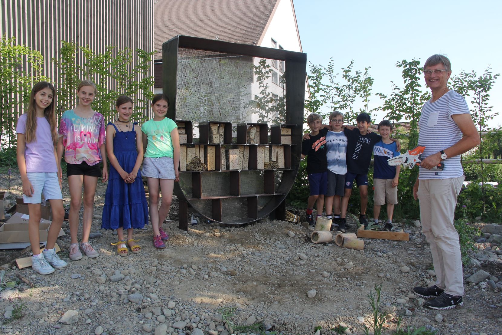 Ein Lehrer posiert mit seinen Schülerinnen und Schülern vor dem neuen Bienenhotel vor der Gemeindeverwaltung.