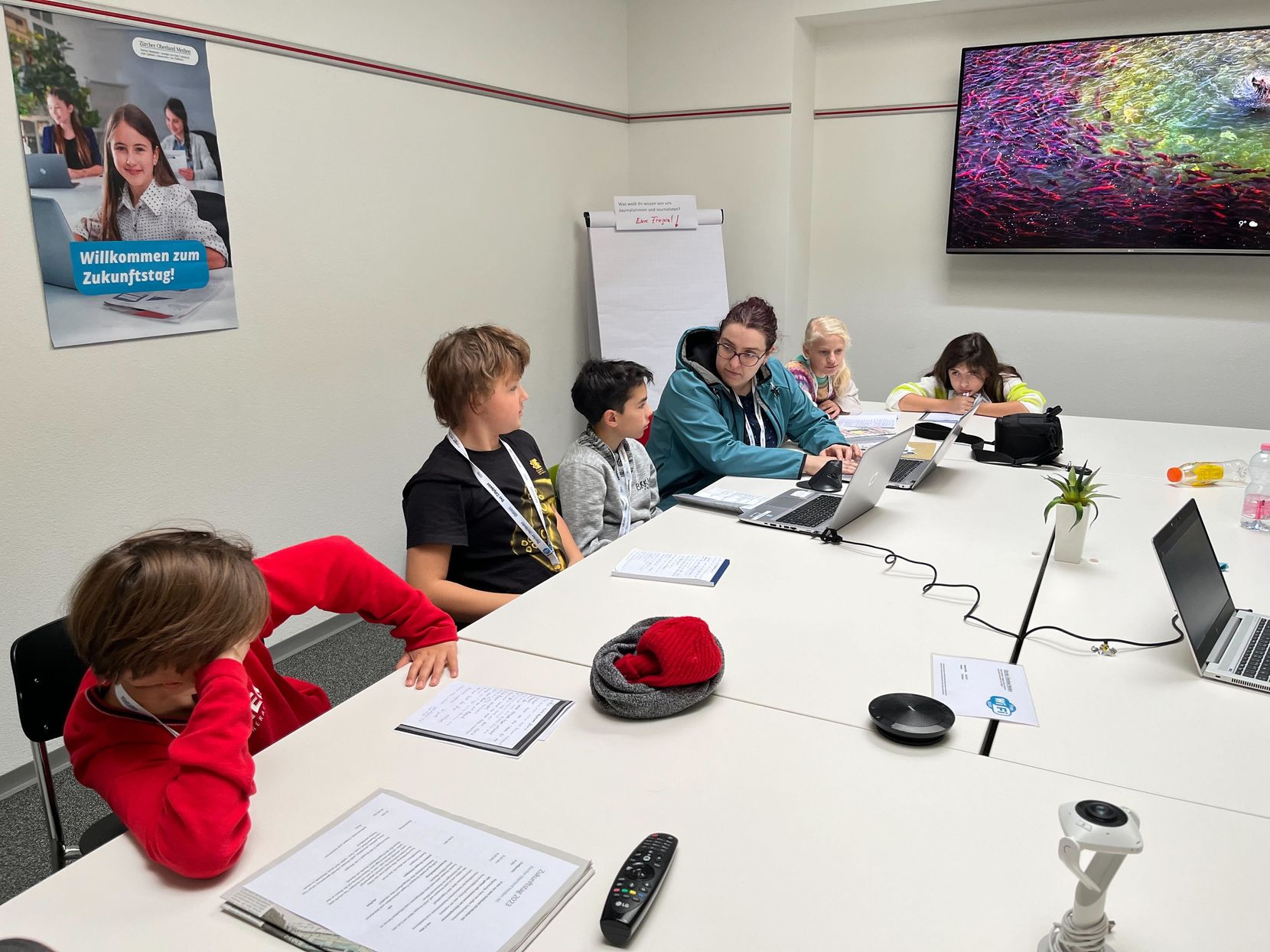 Eine Redaktorin sitzt mit Kindern in einem Sitzungszimmer.
