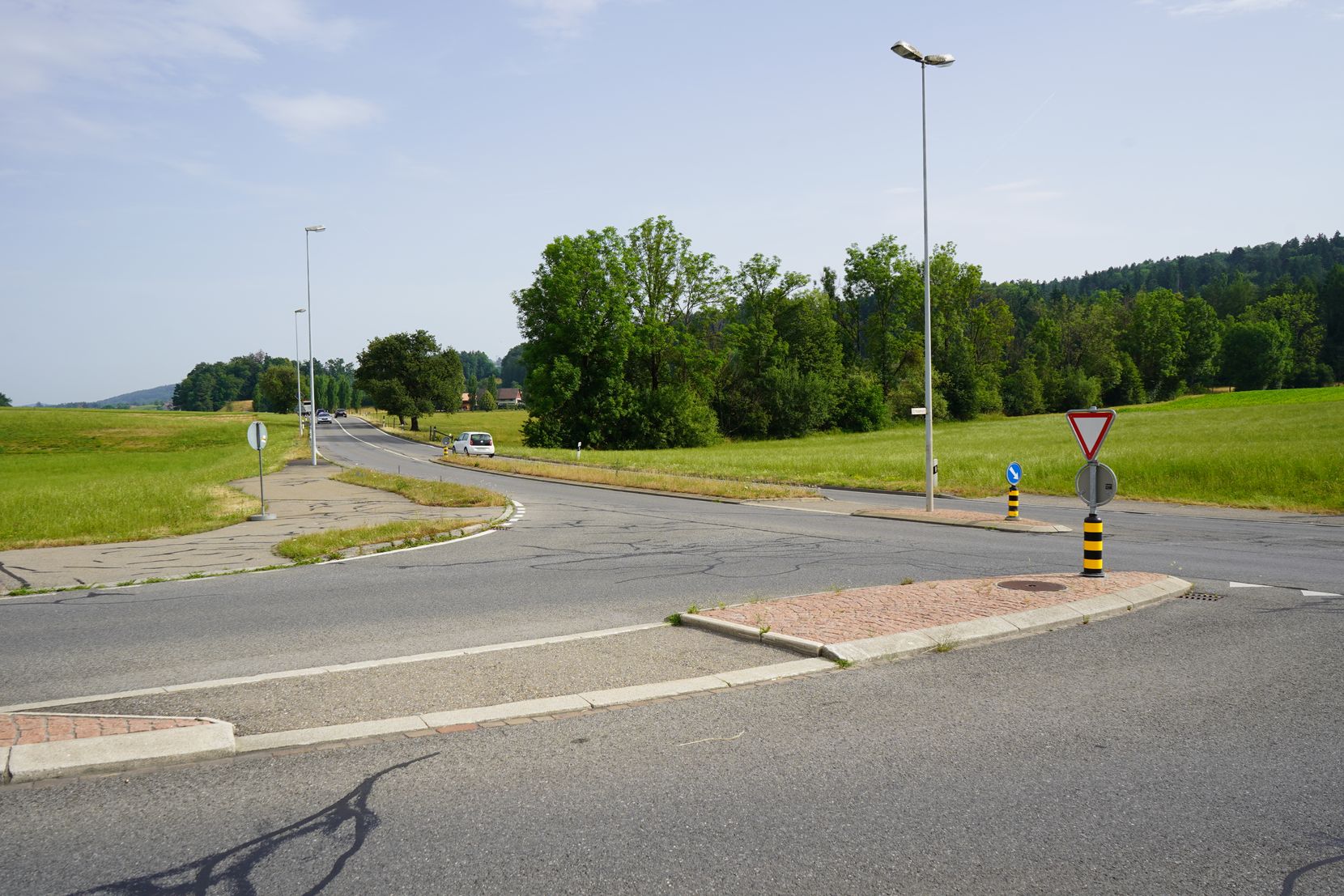 Eine Strassenkreuzung im Sommer, links und rechts der Strasse sind Wiesen zu sehen. 