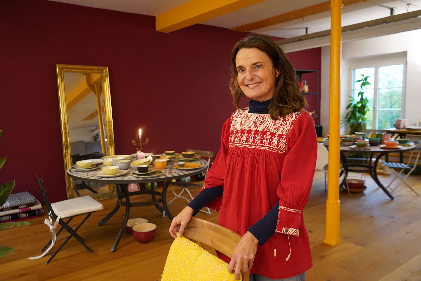 Nicolette Huhn steht hinter einem Stuhl in einem grossen Raum, wo es auch Keramik gibt.