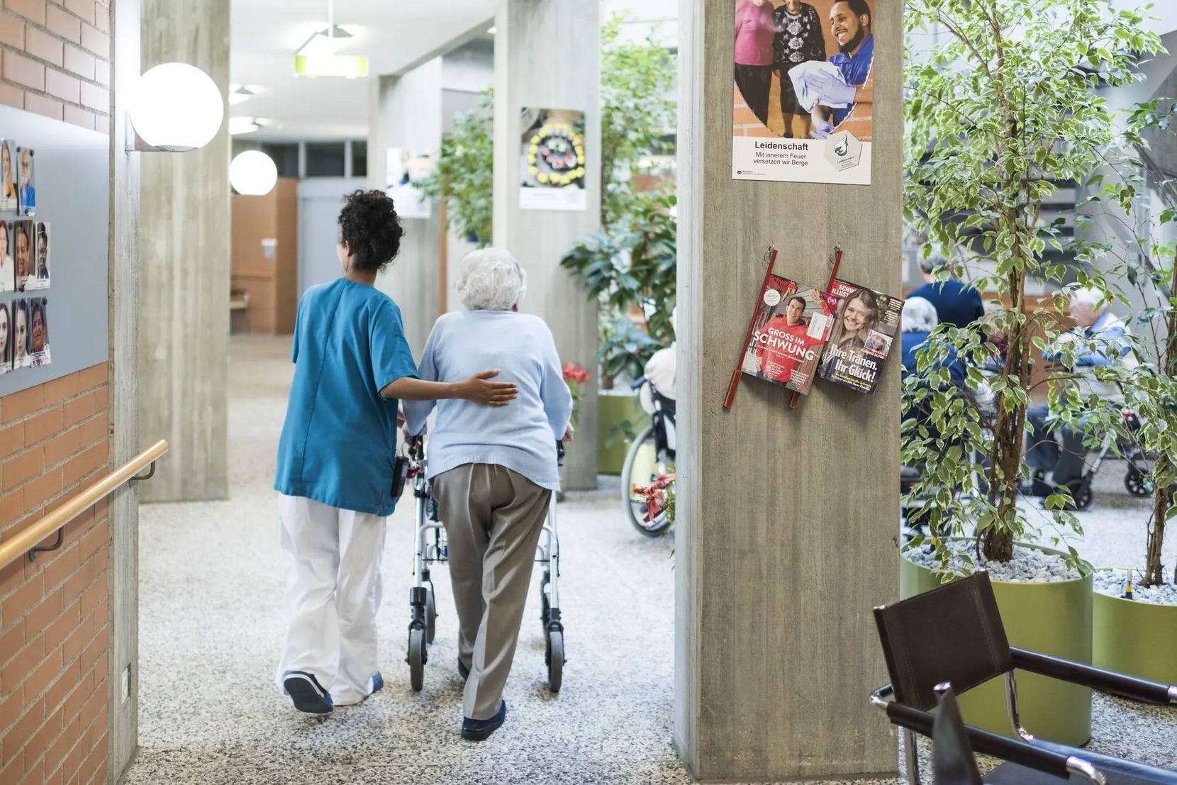 Man sieht eine Pflegeangestellte, die eine Frau mit Rollator begleitet.