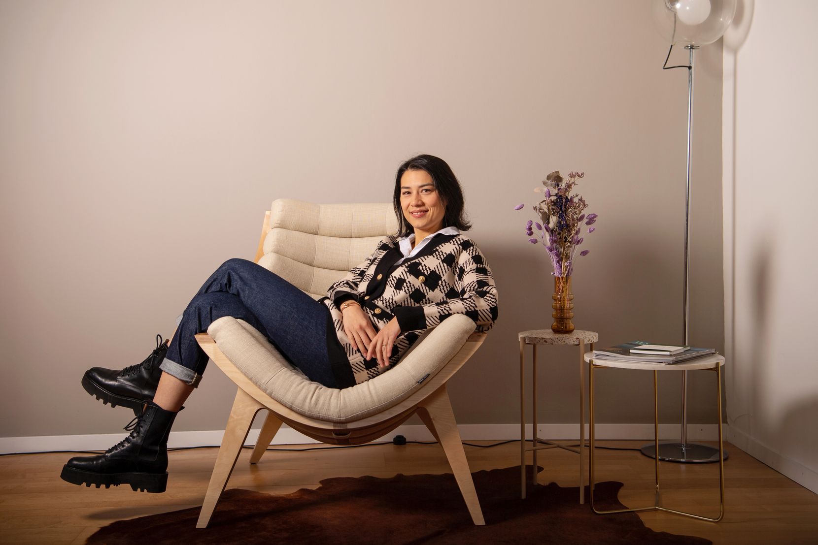 Eine Frau sitzt quer auf einem Sessel mit übereinandergeschlagenen Beinen und lächelt in die Kamera. 