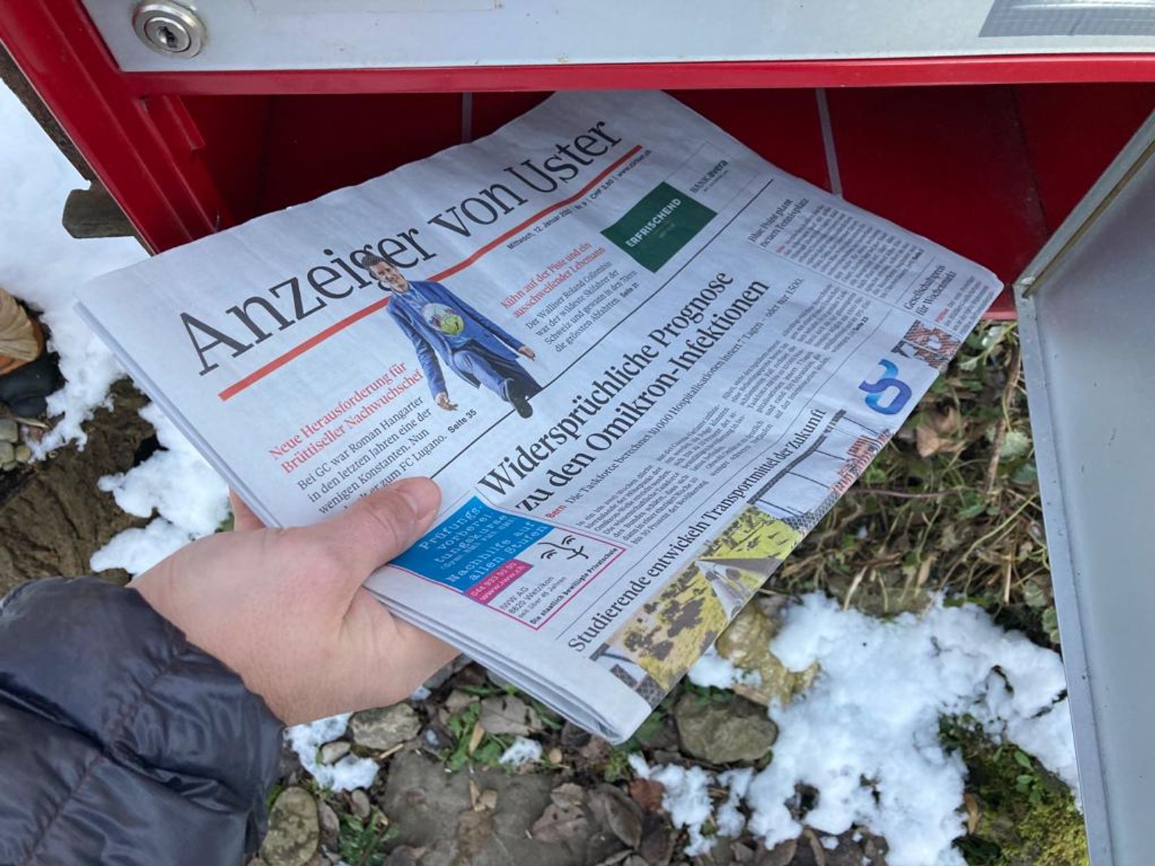 Eine Hand legt eine Zeitung in einen Briefkasten.