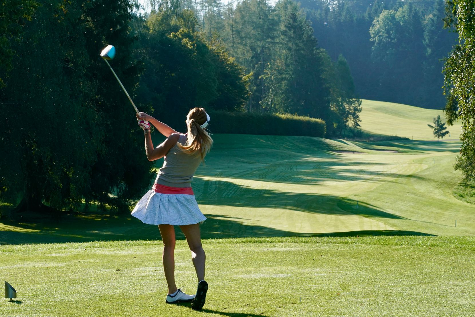 Eine Frau schwingt ihren Golfschläger auf der grünen Wiese eines Golfplatzes.