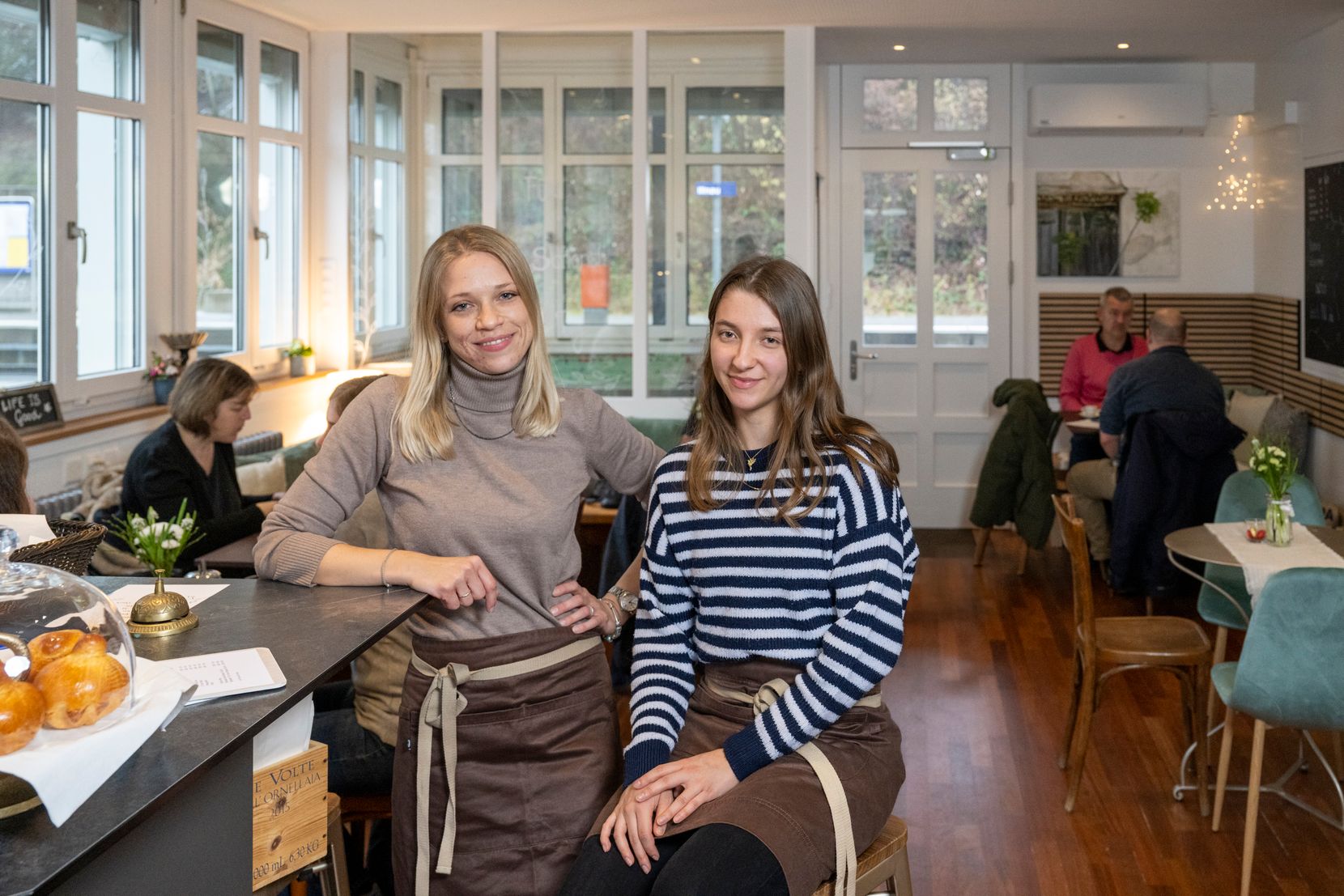 Zwei Frauen lachen in einem Café in die Kamera.