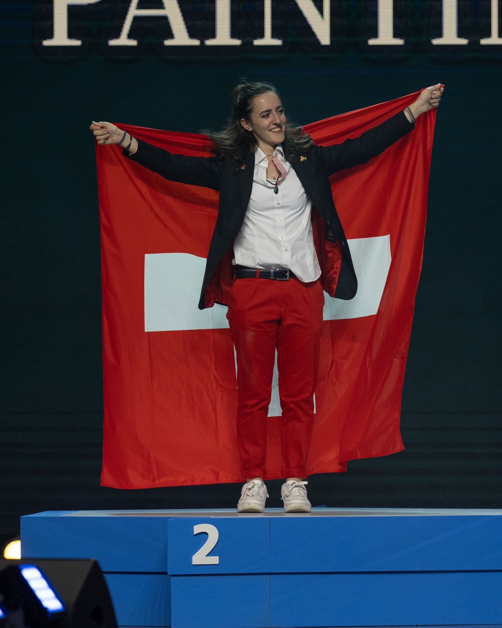 Eine junge Frau steht auf einem Podest und hält eine Schweizerfahne hoch. 