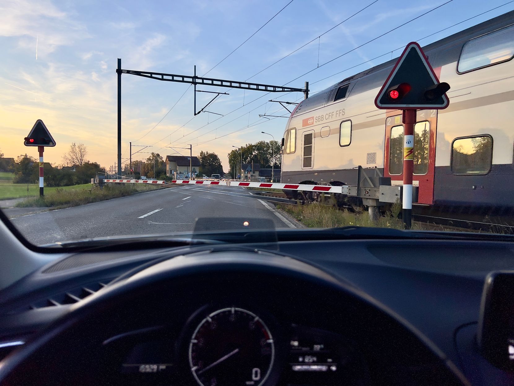 Blick aus einem Auto, dass vor einer Bahnschranke steht, während ein Zug vorbeifährt.