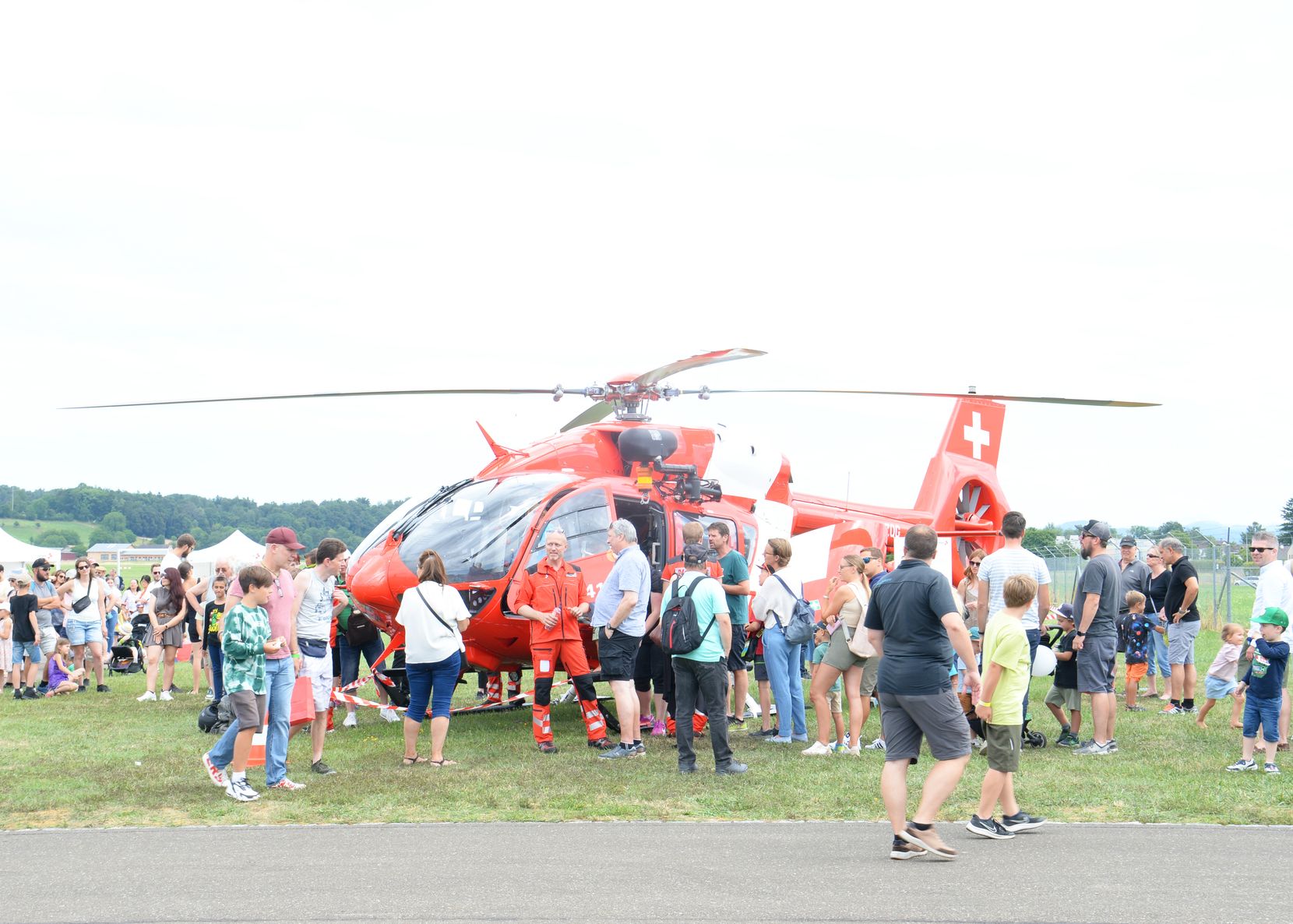 Ein rotweisser Airbus Helikopter H145 der Rega mit vielen Menschen, die ihn bestaunen.