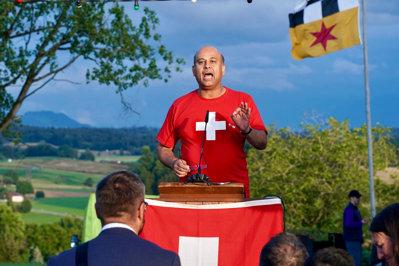 Ein Mann im roten T-Shirt mit weissem Kreuz am Rednerpult.