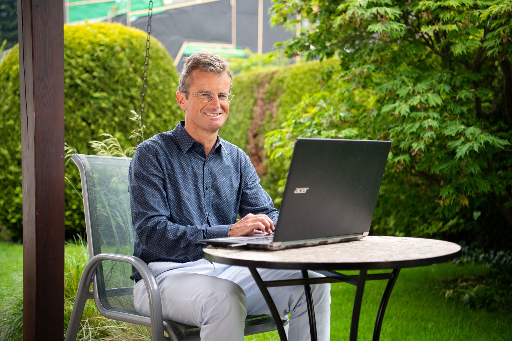 Ein Mann sitzt an einem Gartentisch hinter einem Laptop.