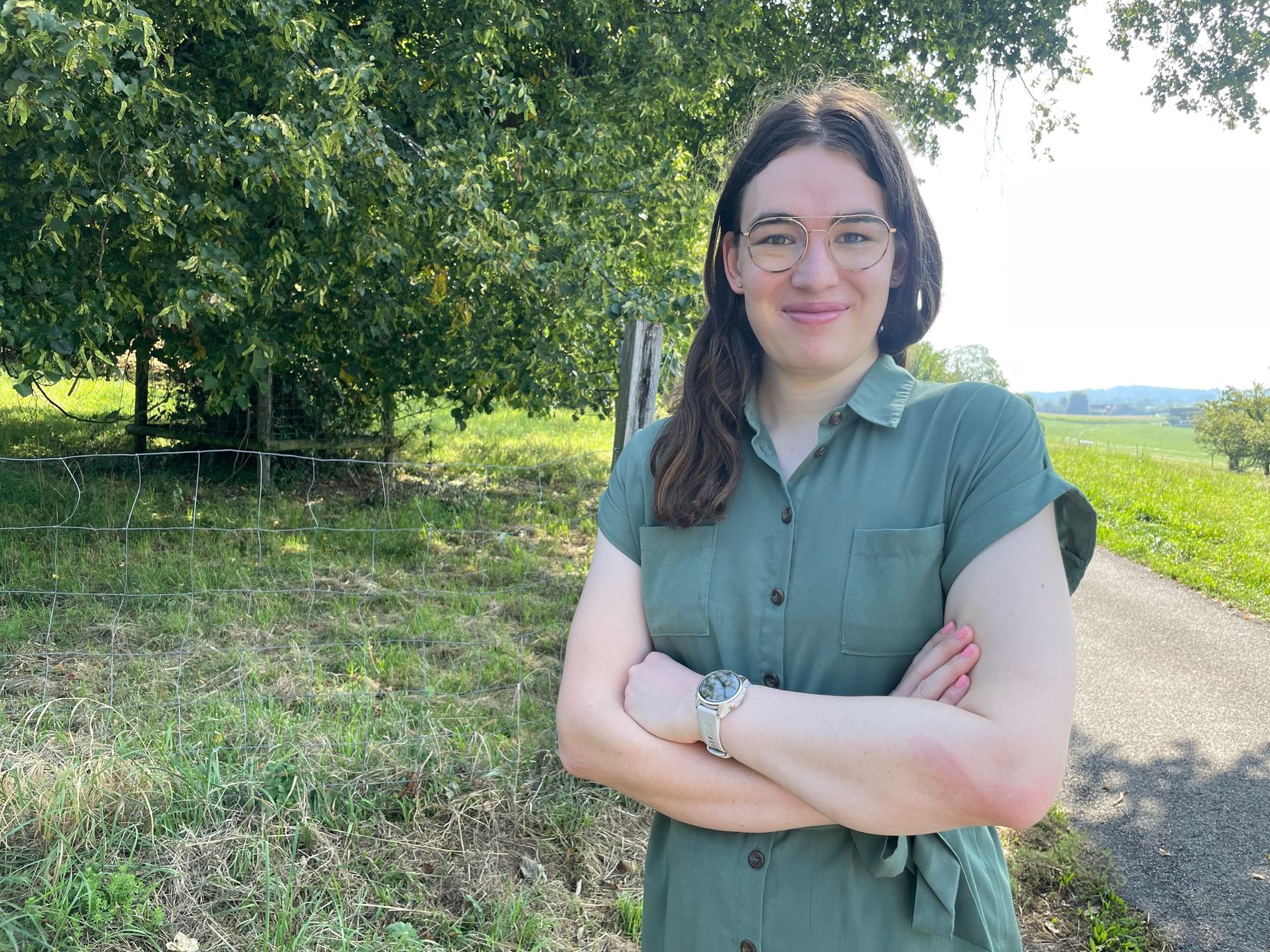 Eine junge Frau mit dunklen Haaren und einer Brille im grünen Kleid.