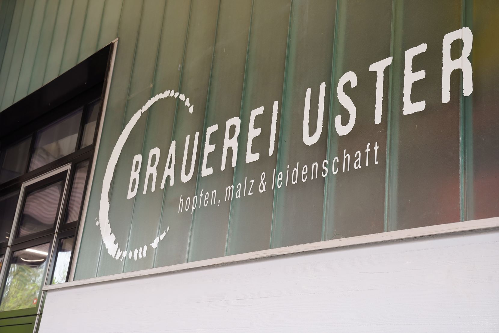 Auf einer Wand sieht man das Logo der Brauerei Uster.