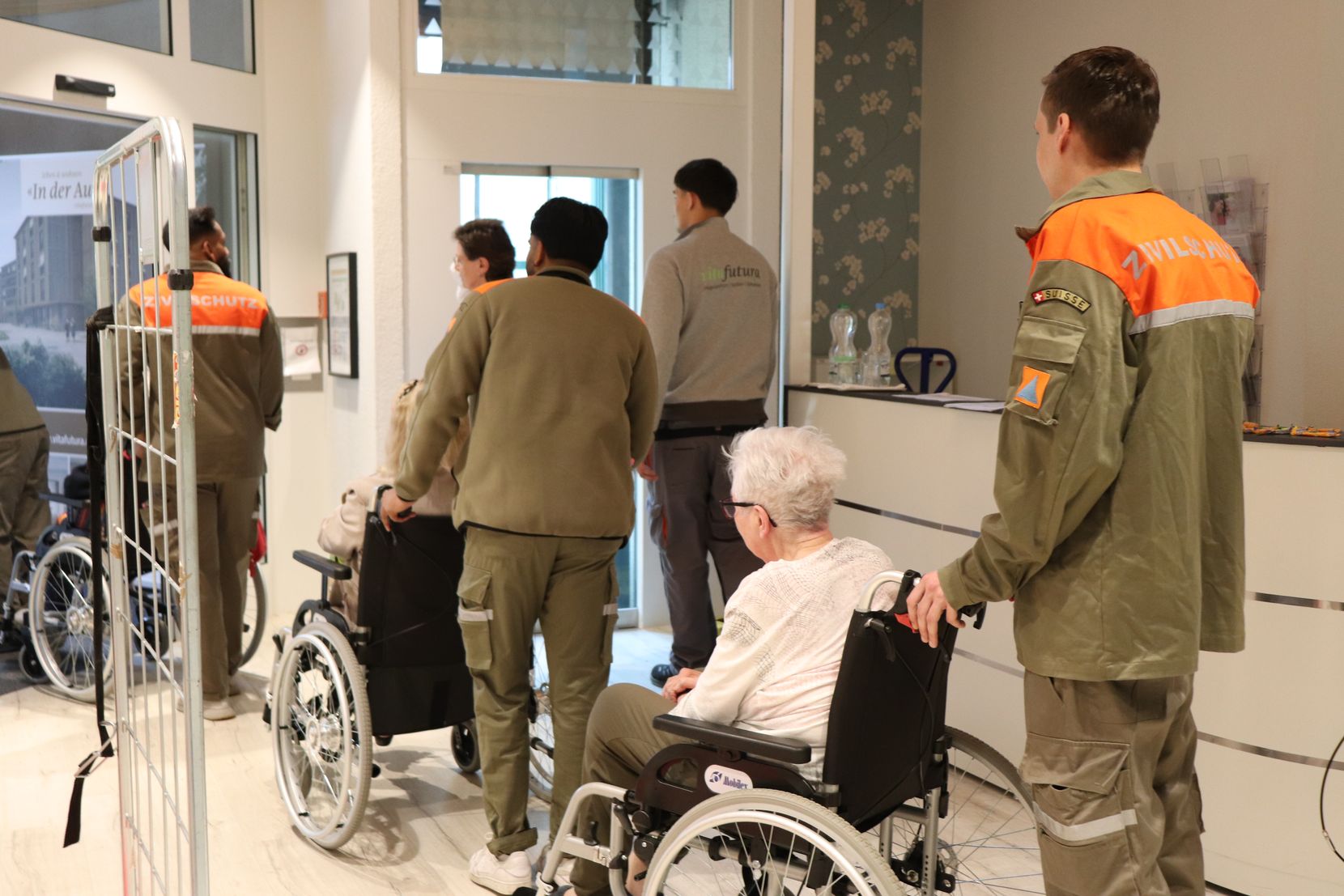 Seniorinnen in Rollstühlen werden von Zivilschützern geschoben. 