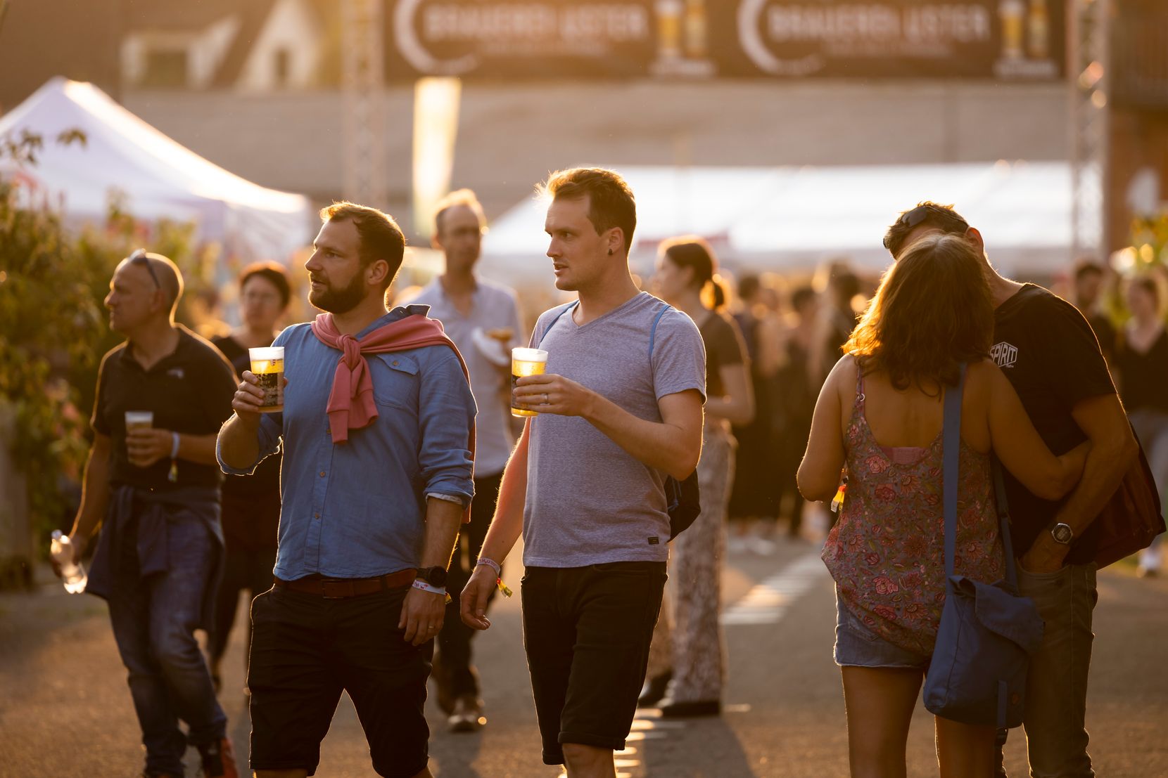 Zwei Männer laufen mit einem Bier in der Hand über ein Festivalgelände.