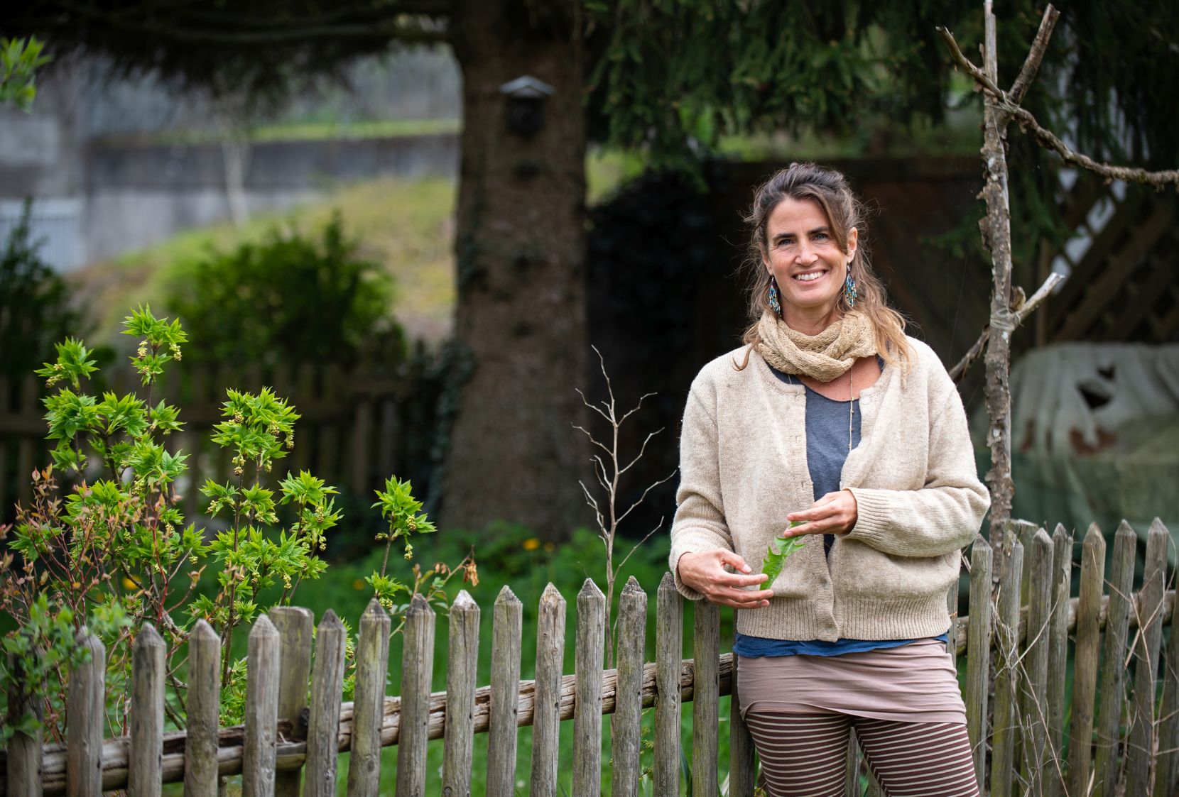 Sarah Zehnder steht vor einem Gartenzaun und hat ein Löwenzahnblatt in der Hand.