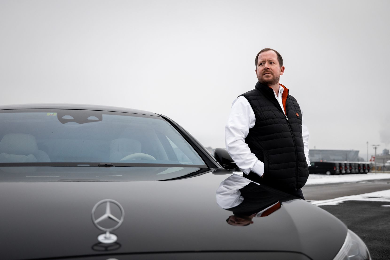 Ein Mann steht neben einem Luxus-Mercedes und blickt in die Ferne.