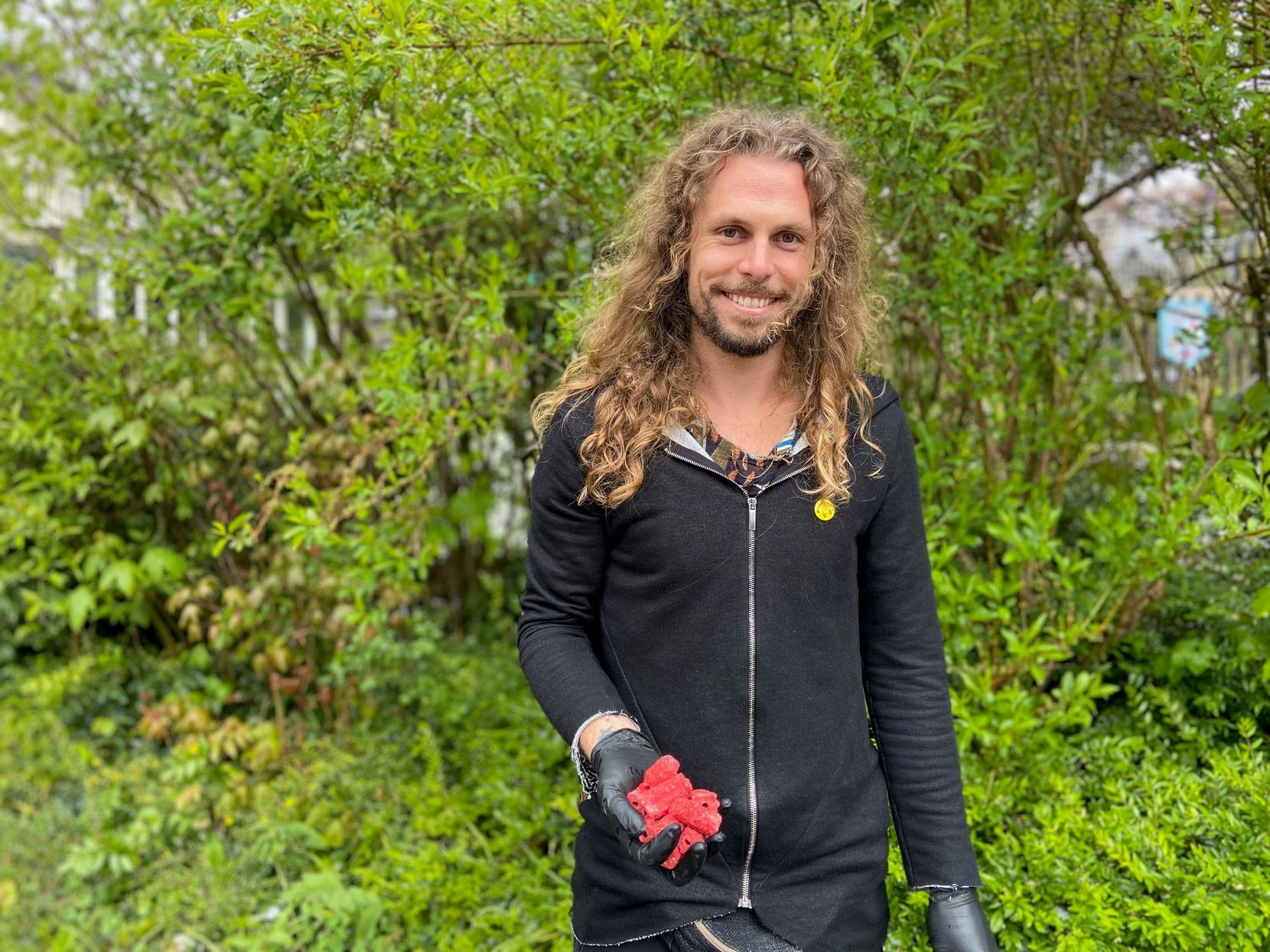 Remo Ronner mit roten Wachsködern in der Hand, er steht vor einem Garten.
