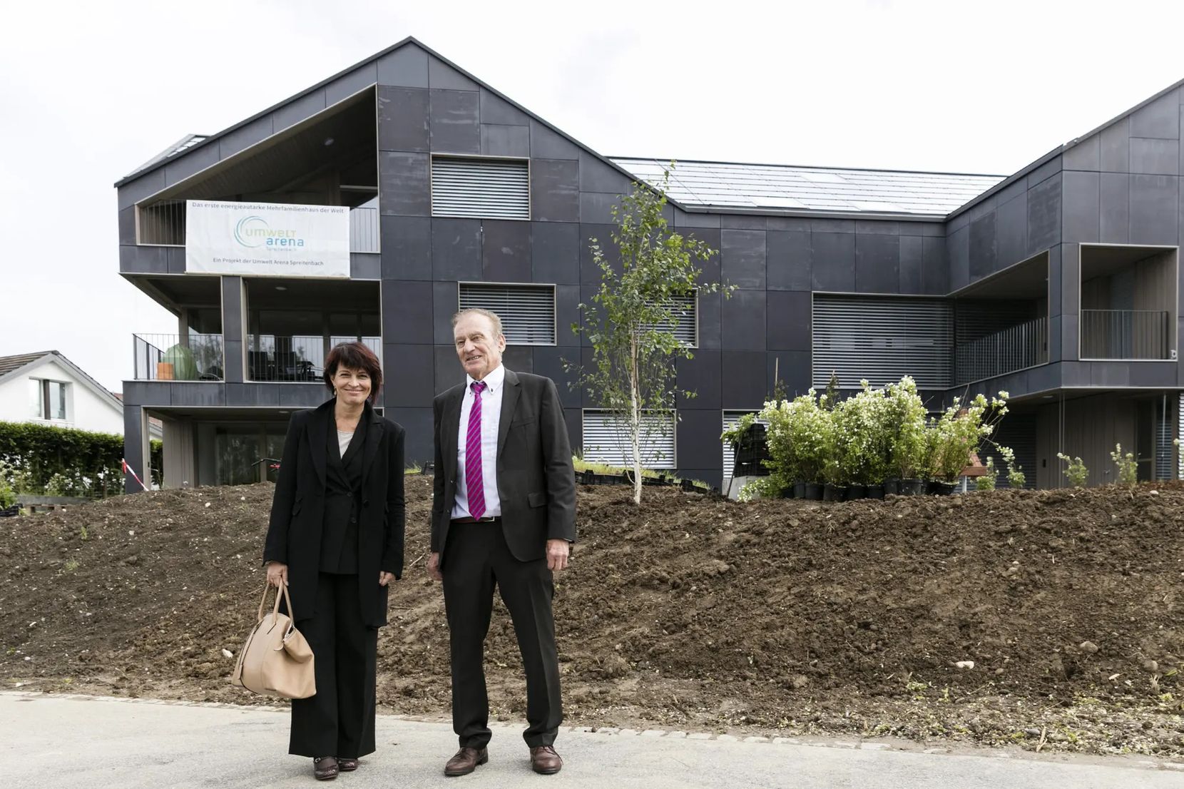 Walter Schmid und die damalige Bundesrätin Doris Leuthard  stehen 2016 vor einem Haus mit PV-Panels in der Fassade.