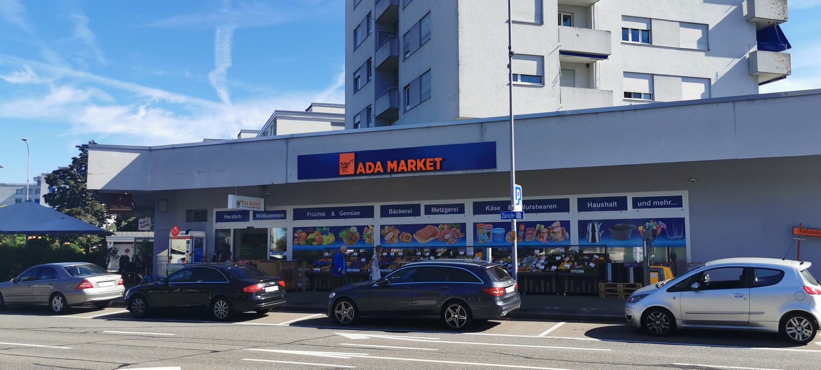 Ein Teil der Wilstrasse in Dübendorf mit dem Ada Market und parkierten Autos.