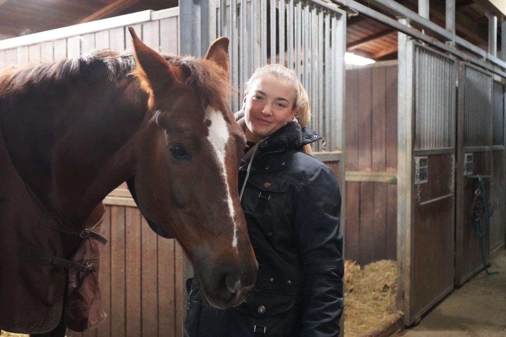 Leonie Linsbichler posiert im Stall mit einem Pferd.