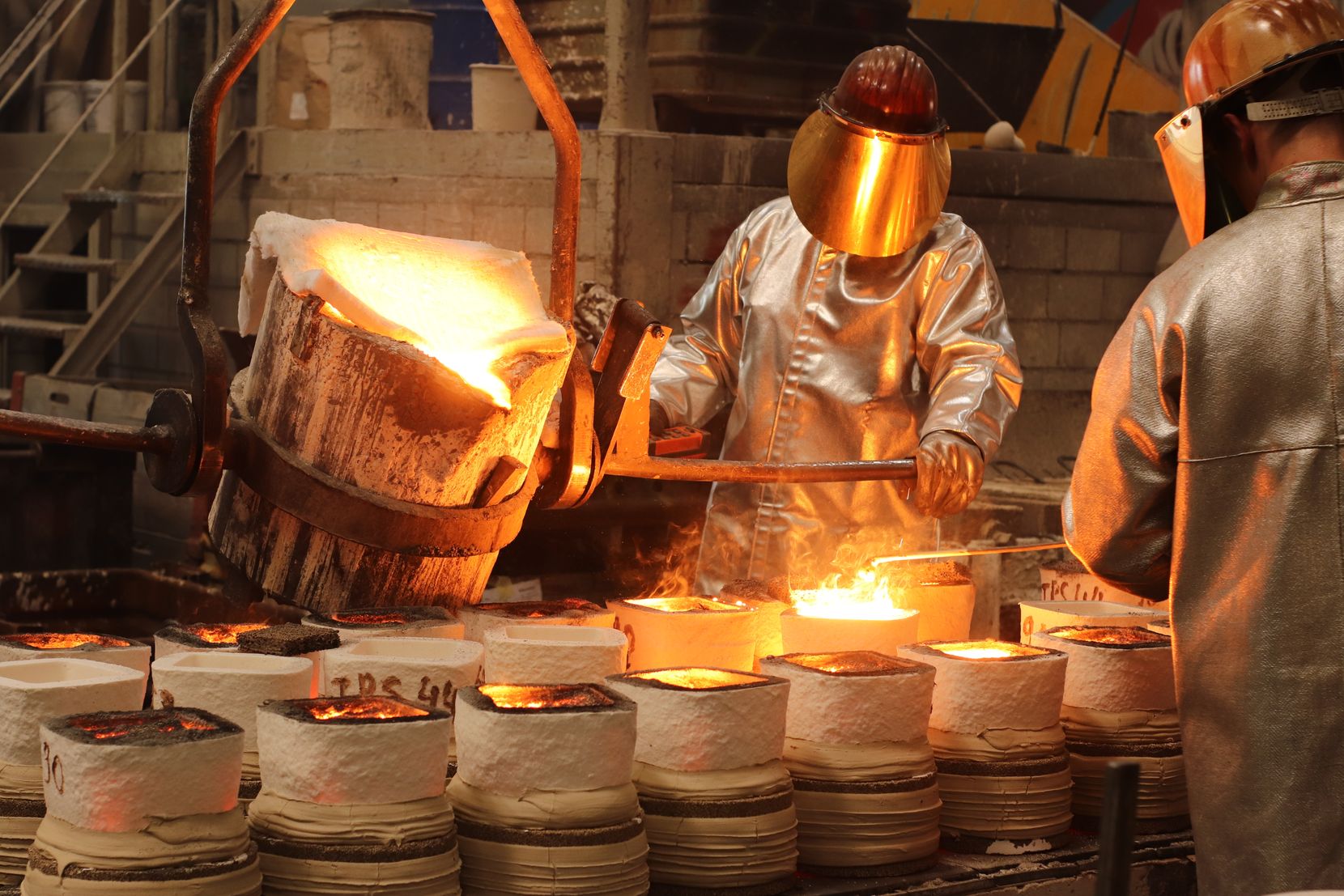 Arbeiter giessen flüssiges Metall in Gussformen.