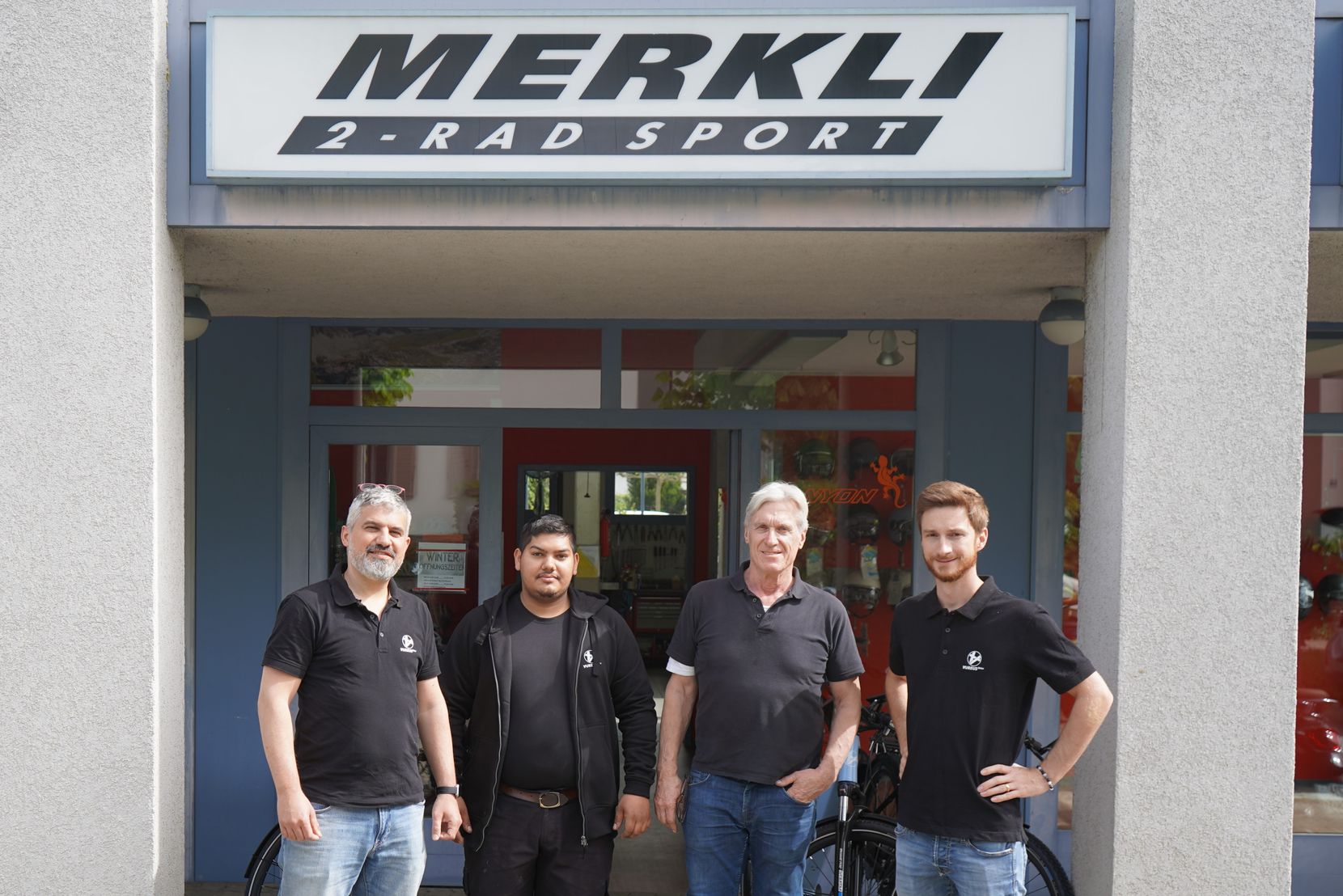 Gruppenbild mit vier Männern vor dem Eingang zu Merkli 2-Rad Sport in Wetzikon.