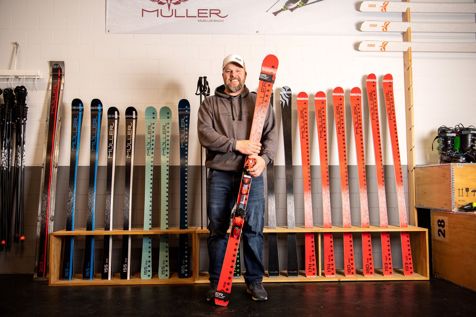 Ein Mann steht mit einem Paar Skis in der Hand vor noch mehr Skis.