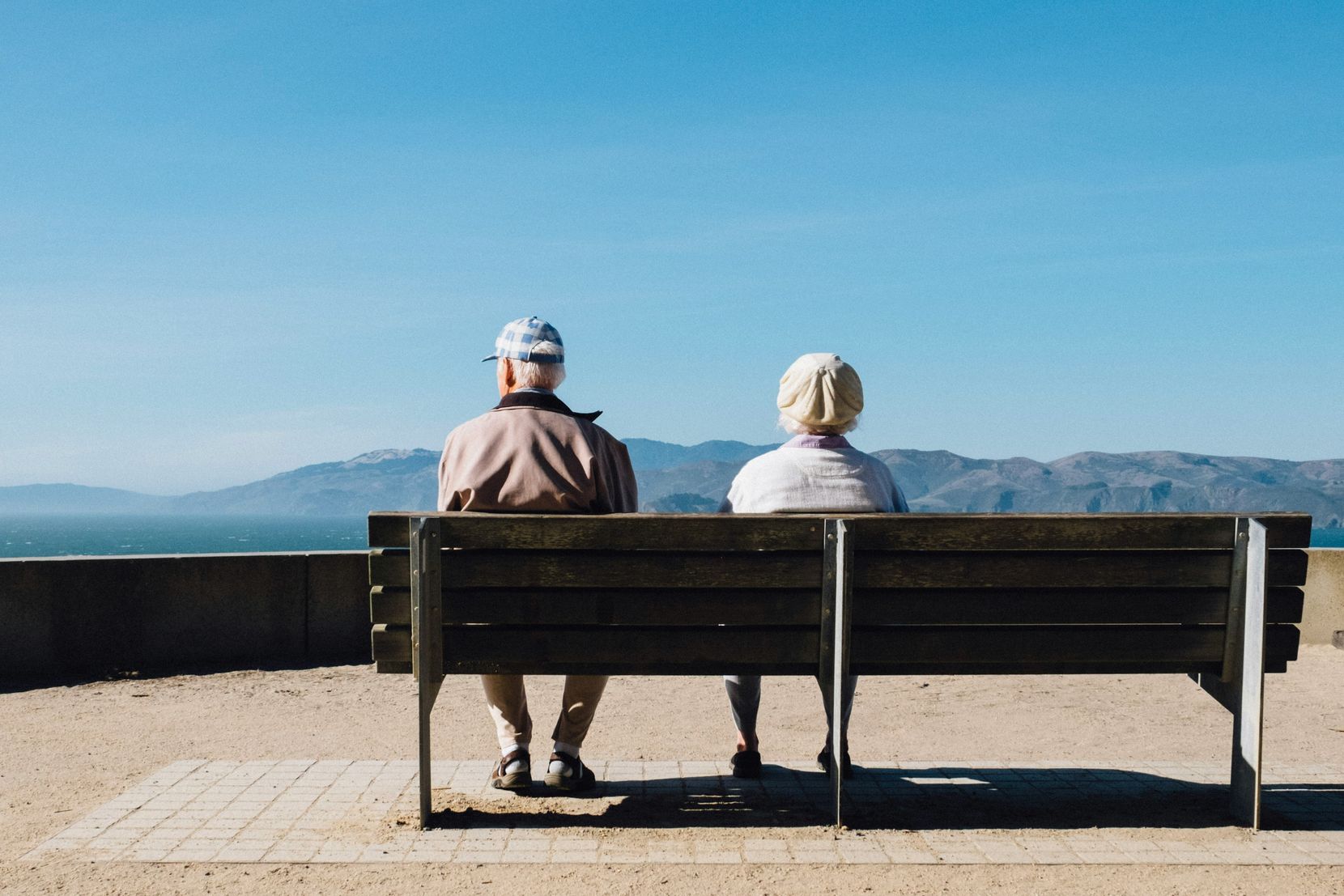 Ein altes Paar auf einer Bank, von hinten fotografiert.