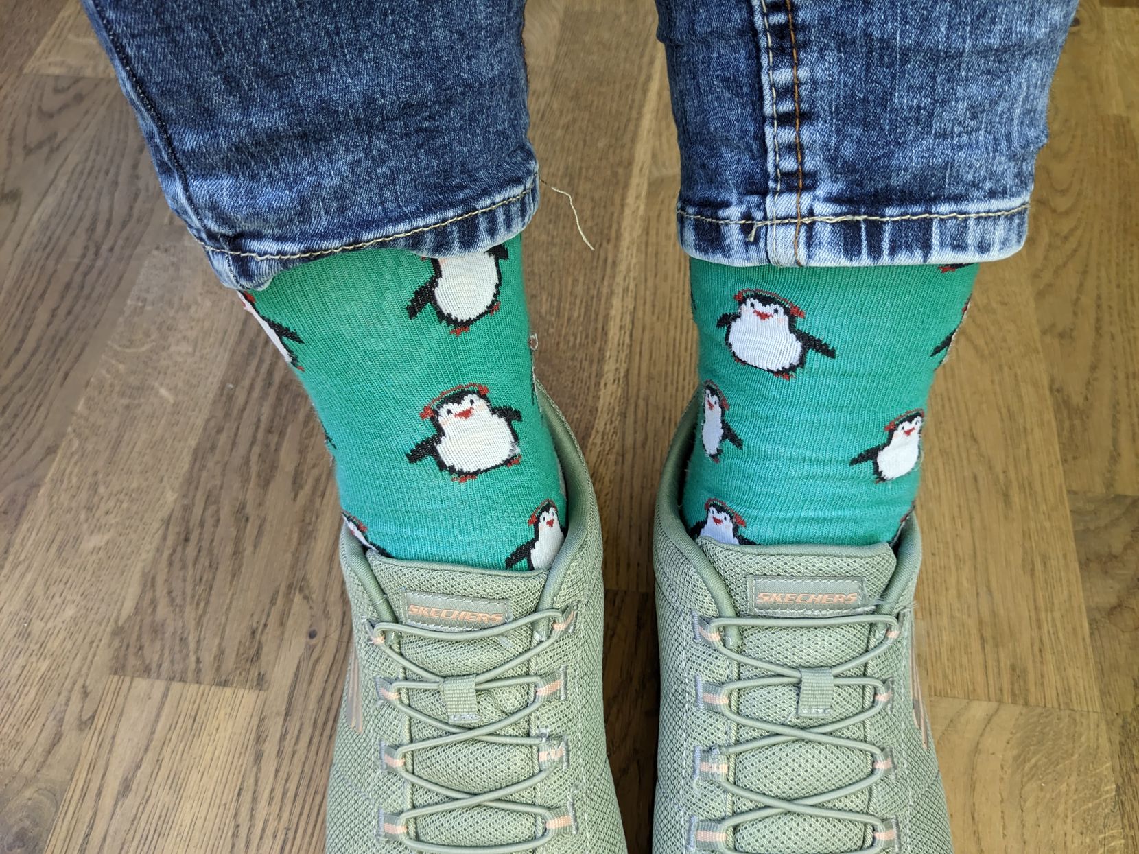 Man sieht Socken mit Pinguinen in grünen Schuhen.
