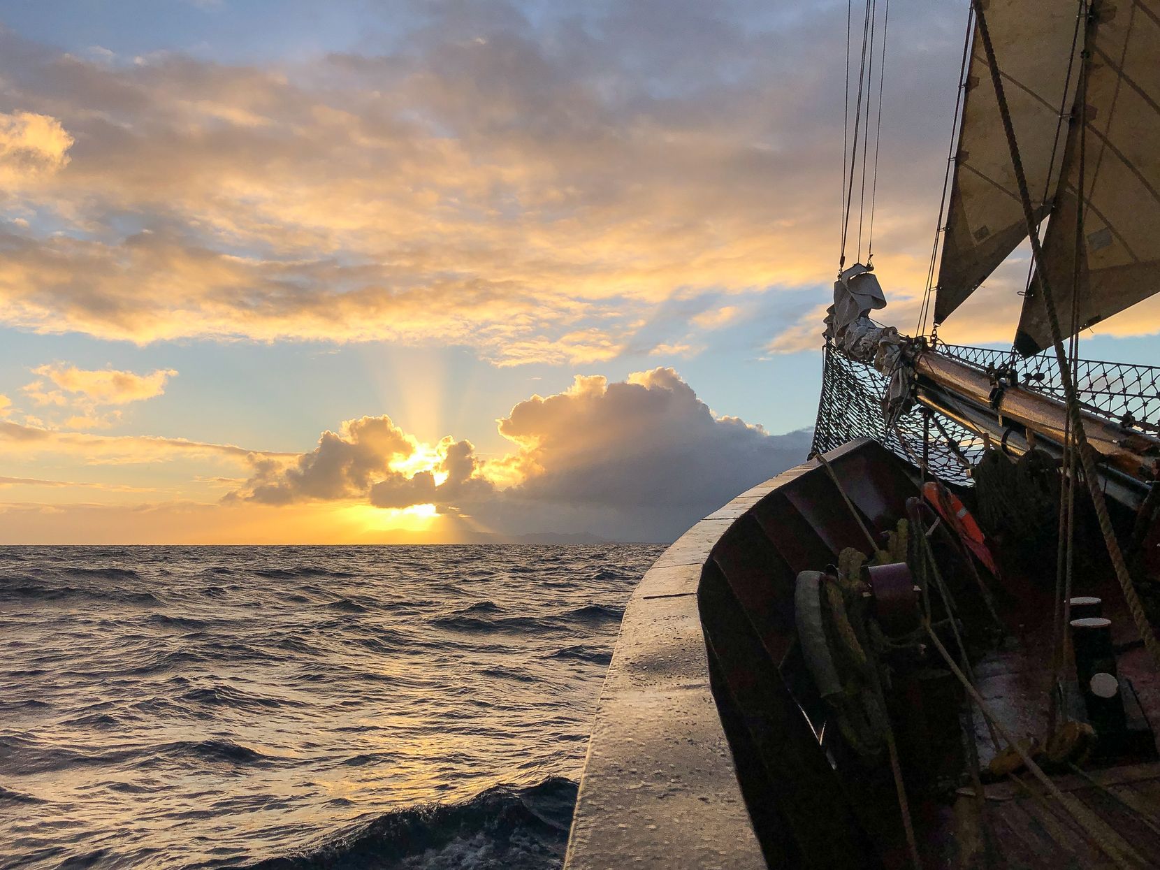 Man sieht den vorderen Teil eines Segelschiffs, mit Blick auf den Sonnenaufgang.