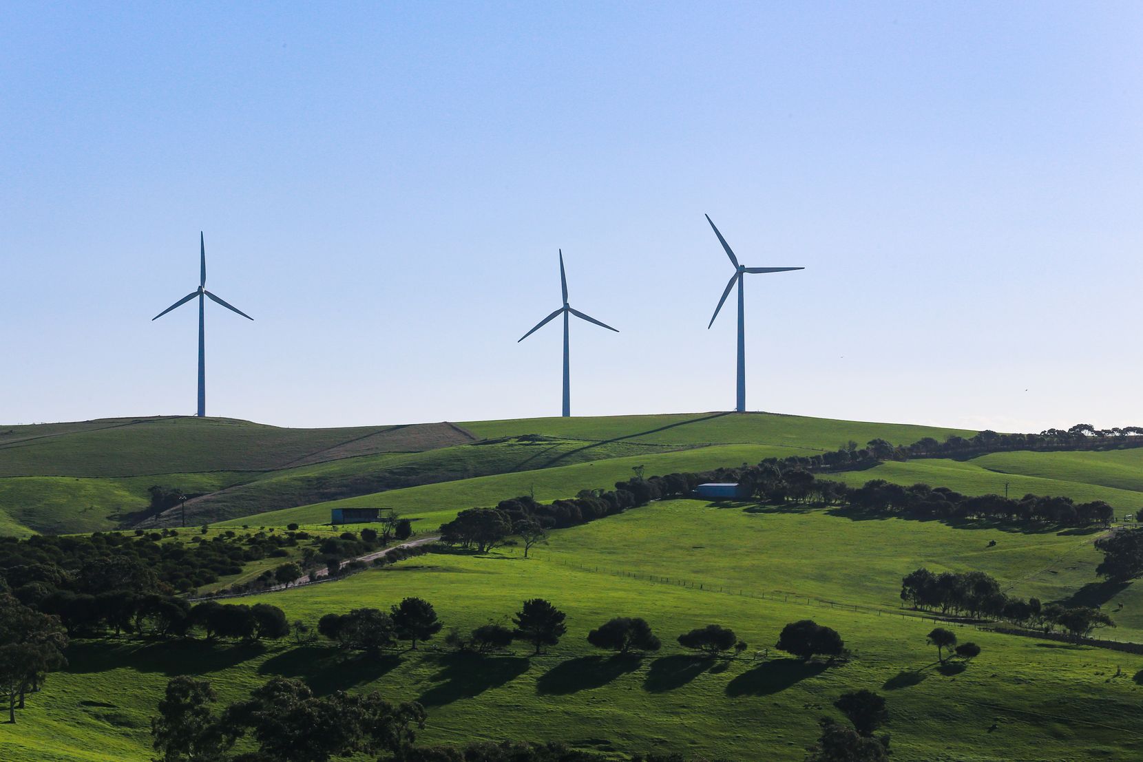 Man sieht drei Windräder auf einem grünen Hügel.